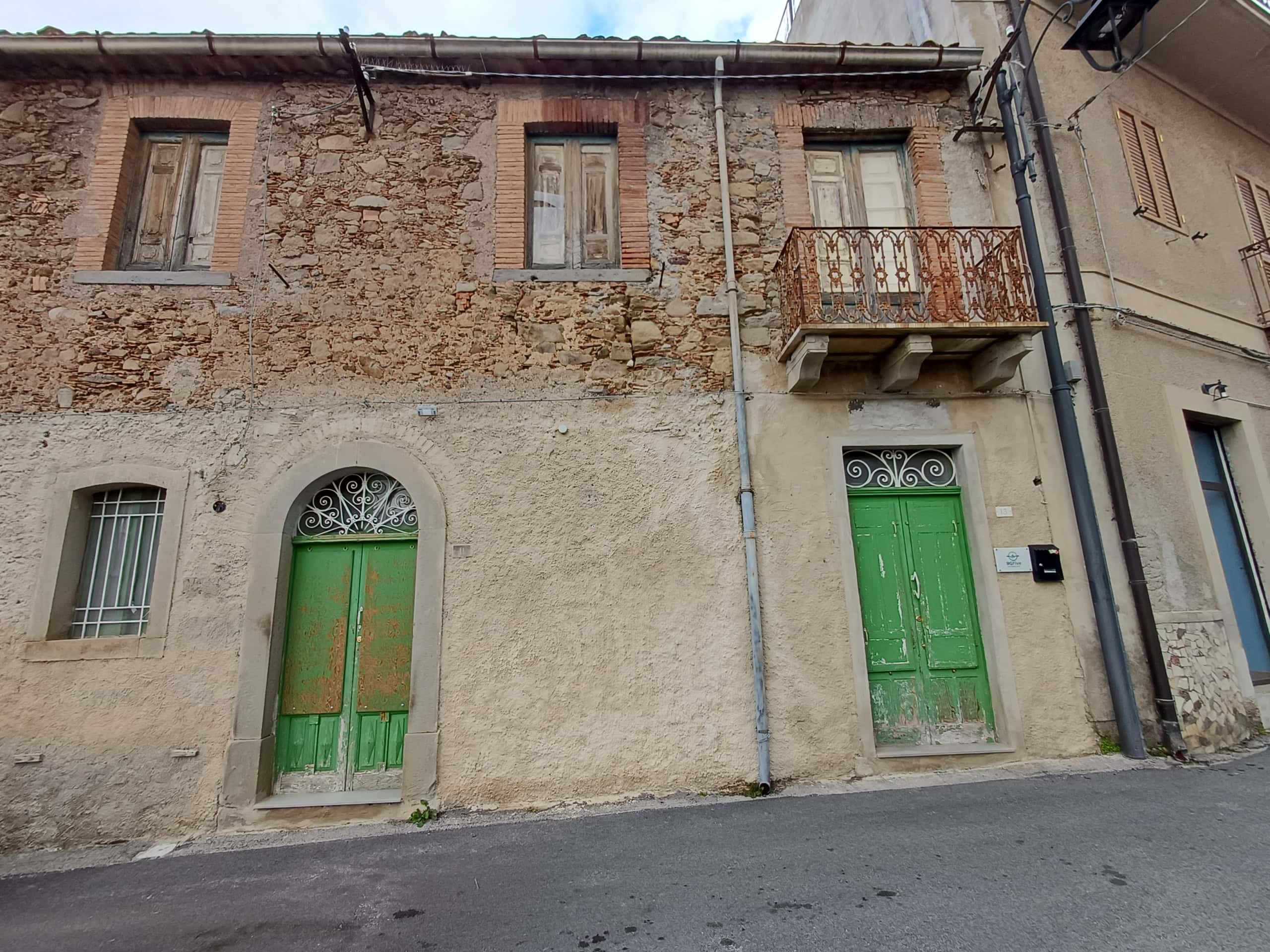Anticamera di un edificio storico con porte verdi e balcone in ferro battuto, situato in una strada urbana. Edificio con pareti in pietra e intonaco, caratteristico del centro storico italiano.