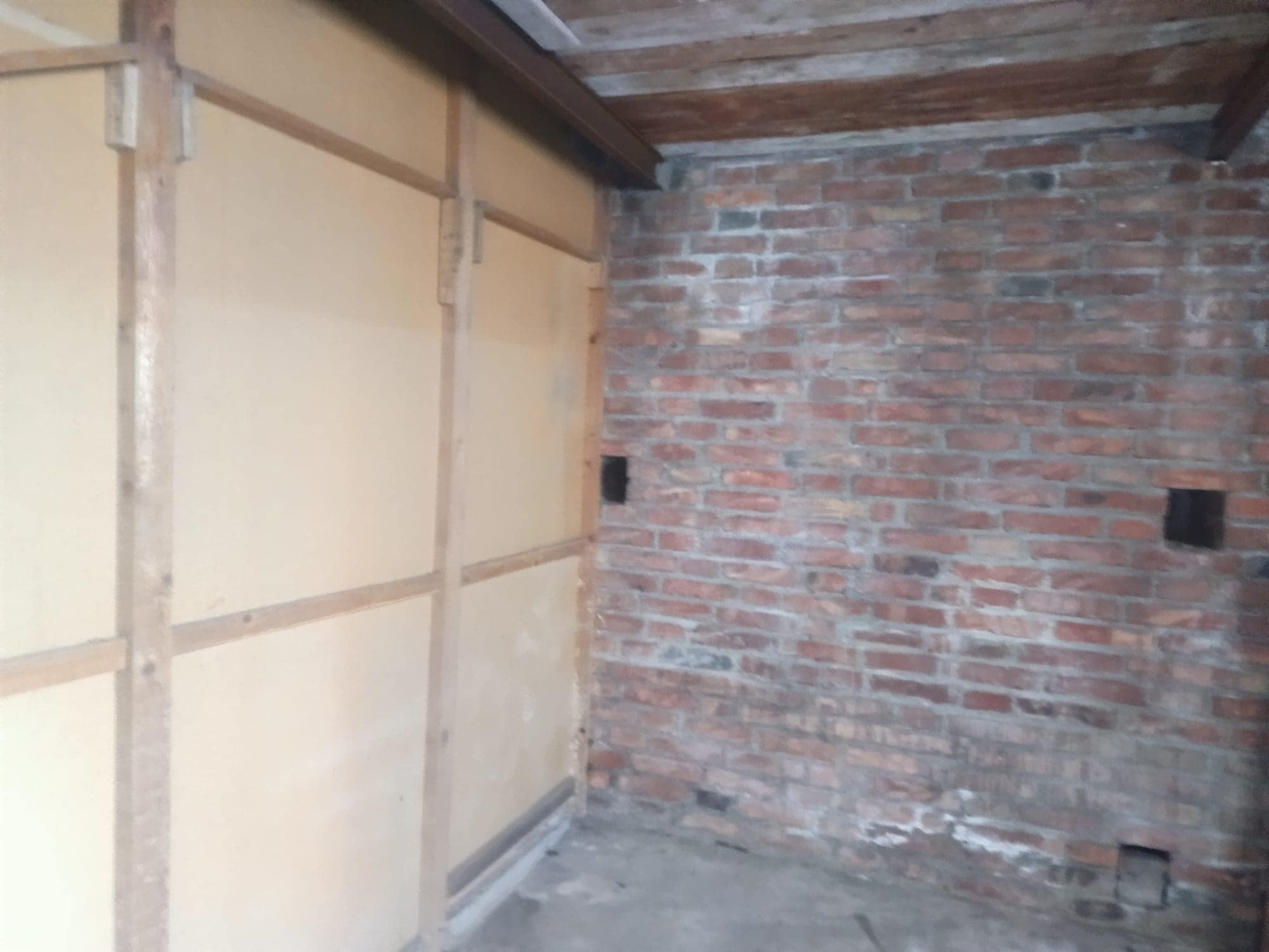 Il muro in mattoni rossi e la parete in cartongesso in fase di ristrutturazione di un appartamento, con elementi di costruzione visibili e lavori in corso.