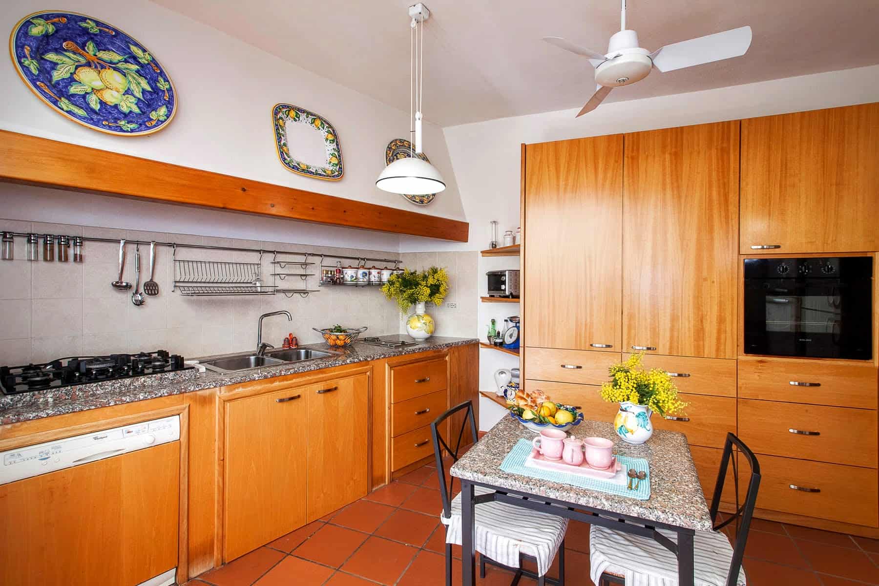 Lavagna da cucina in stile rustico con mobili in legno, piano di lavoro in granito, e accessori decorativi colorati, ideale per una casa accogliente e funzionale.