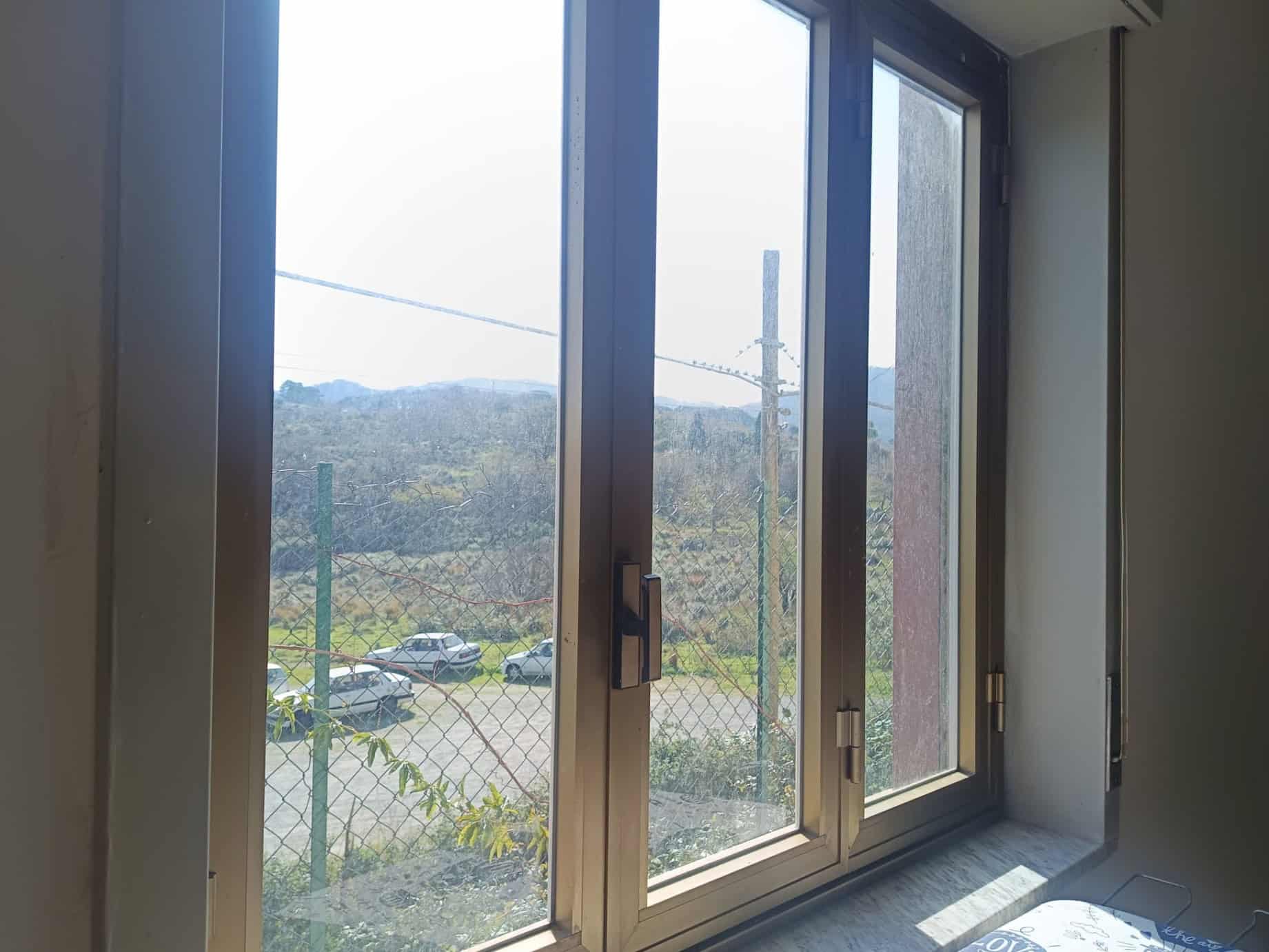 Vetrata scorrevole in alluminio con vista su paesaggio naturale e area esterna recintata, ideale per ambienti moderni e luminosi.