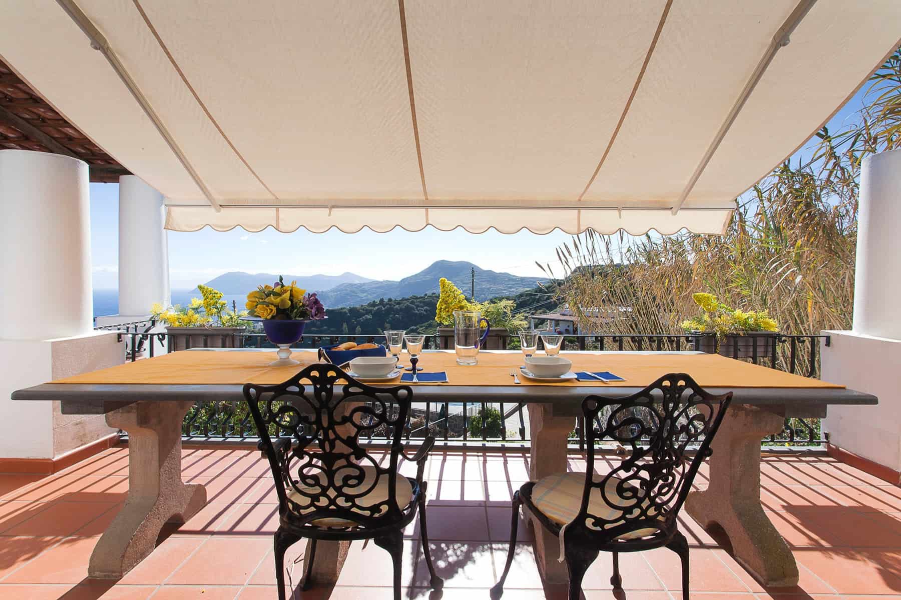 Vista panoramica dal terrazzo di una casa con tavolo e sedie, montagne e cielo sereno sullo sfondo, ambiente esterno elegante e accogliente.