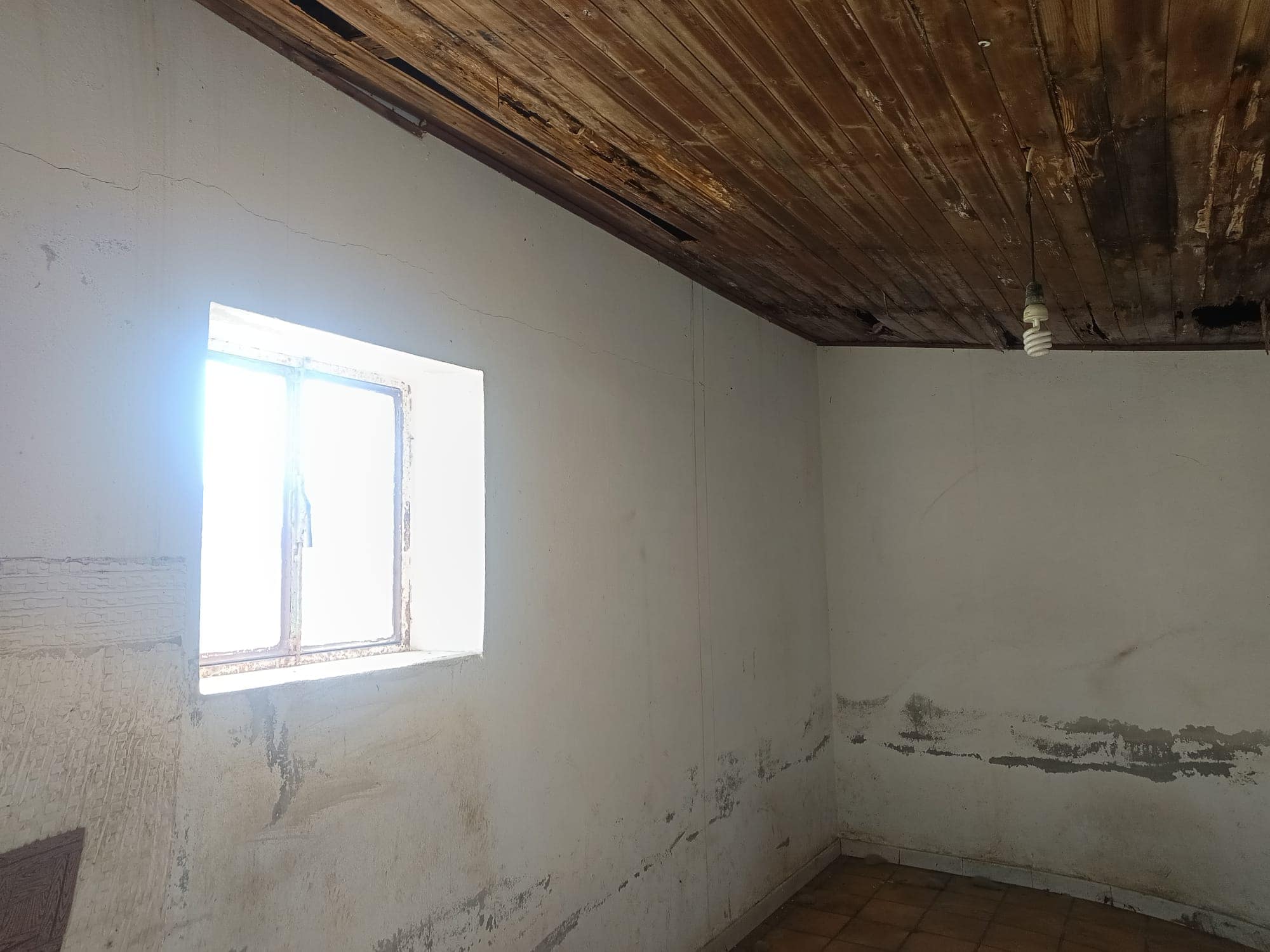 Pannello di parete in una stanza in fase di ristrutturazione con pareti bianche e soffitto in legno, luce naturale che entra dalla finestra.