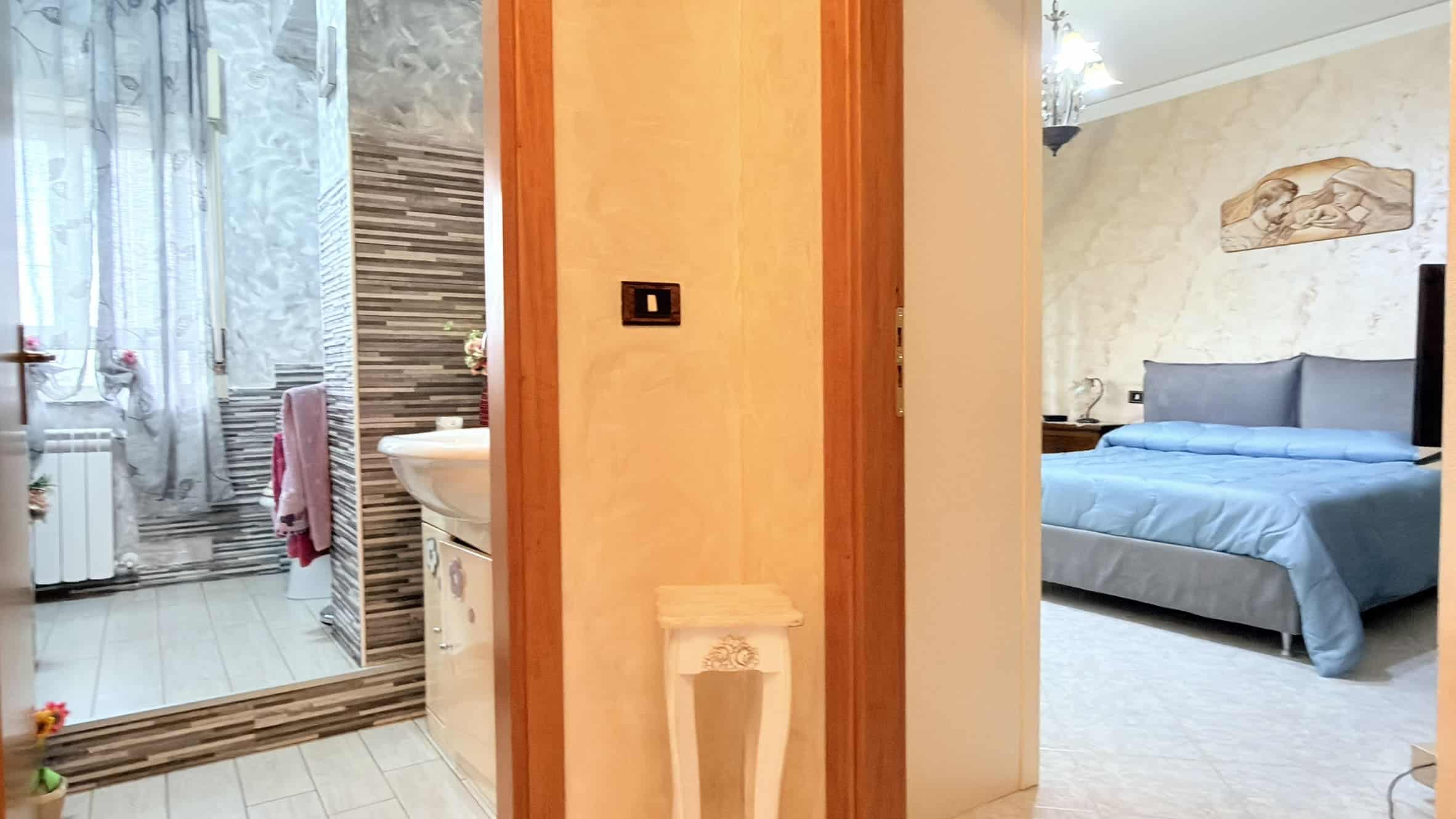 Specchio e porta scorrevole in vetro che separano il bagno dalla camera da letto, con arredi moderni e dettagli eleganti, ideale per soluzioni abitative di alta qualità.