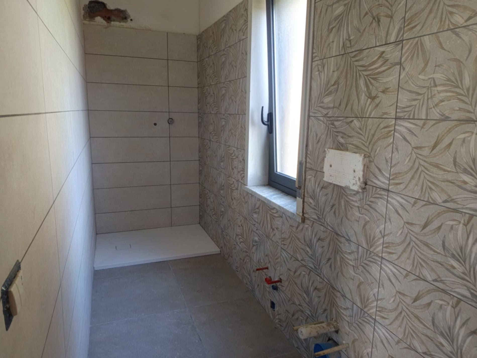 Ampia stanza in fase di ristrutturazione con pareti rivestite di piastrelle decorative e finestra grande per illuminazione naturale.