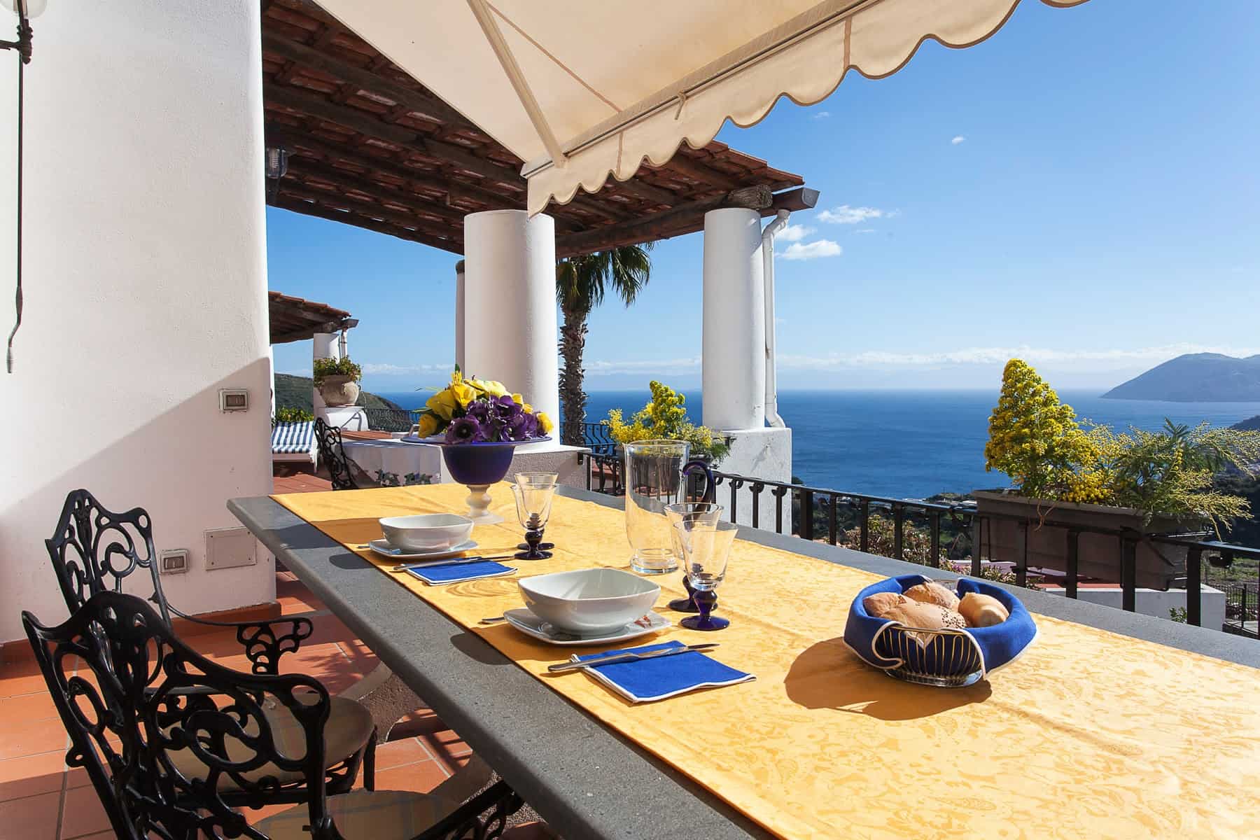 Vista panoramica dal terrazzo con tavolo apparecchiato, vista mare e colline, ideale per pranzi all'aperto e momenti di relax in un ambiente elegante e accogliente.