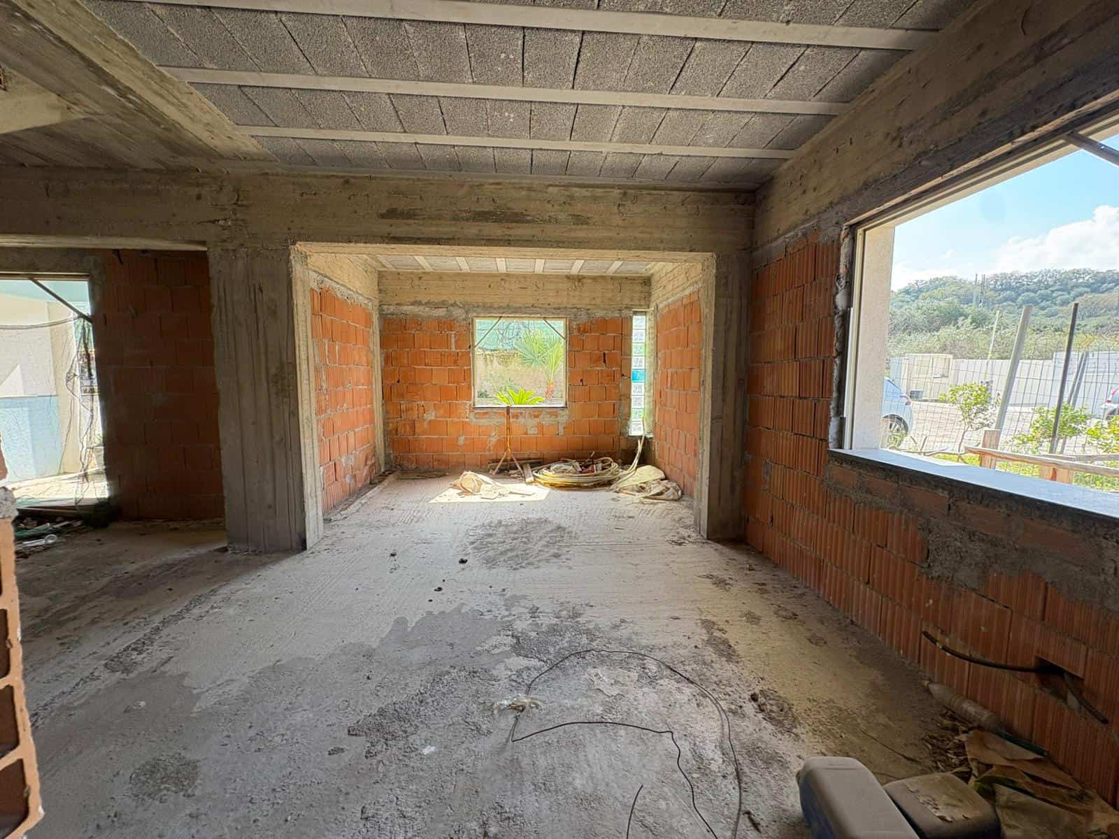 Aggiunta di un'immagine di un interno di una casa in costruzione con pareti in mattoni e grandi finestre che offrono una vista panoramica sulla campagna circostante.
