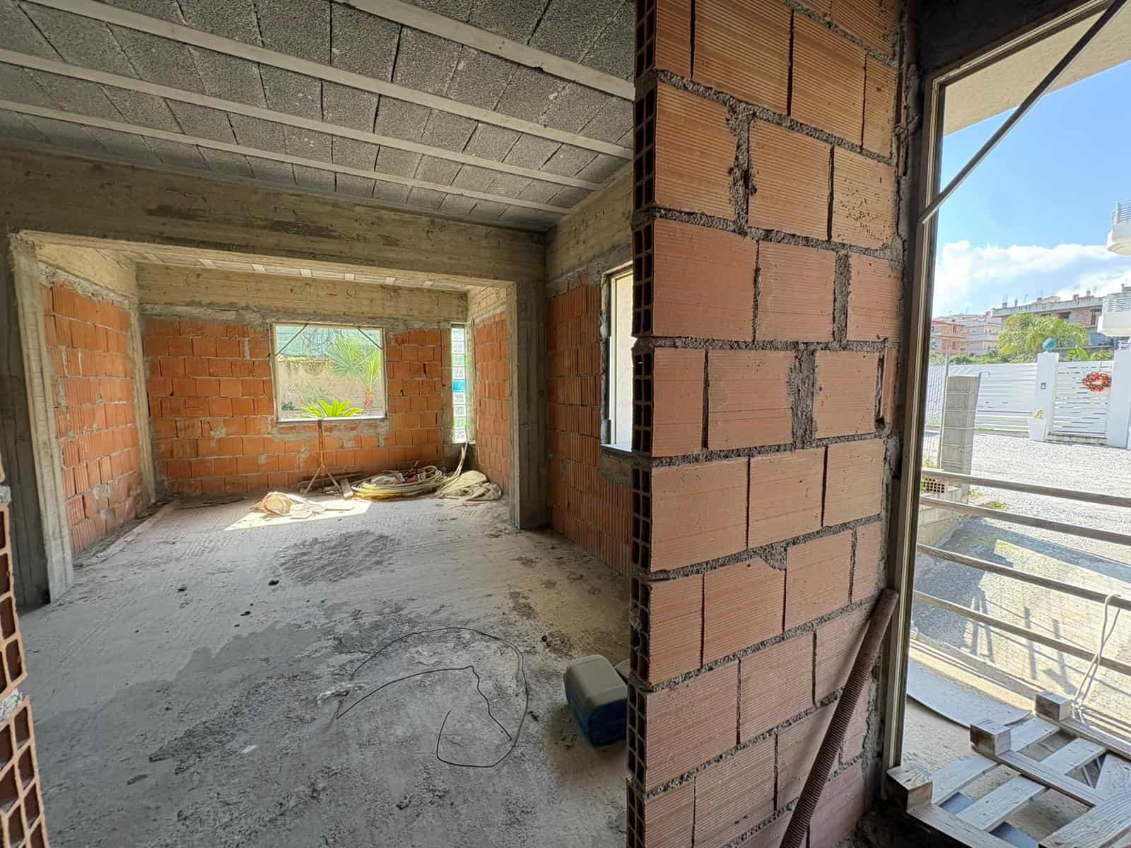 Interno di un appartamento in costruzione con pareti in mattoni e grandi finestre, pronto per finiture e arredi.
