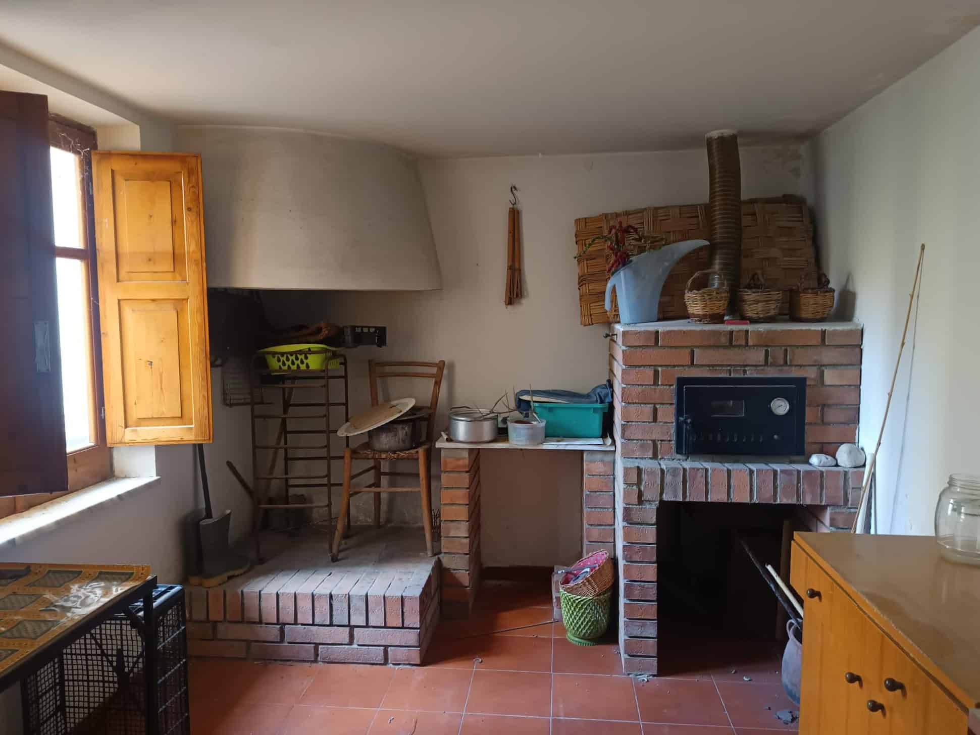 Antico camino in pietra e mattoni in una cucina rustica con mobili in legno, ambiente accogliente e tradizionale.