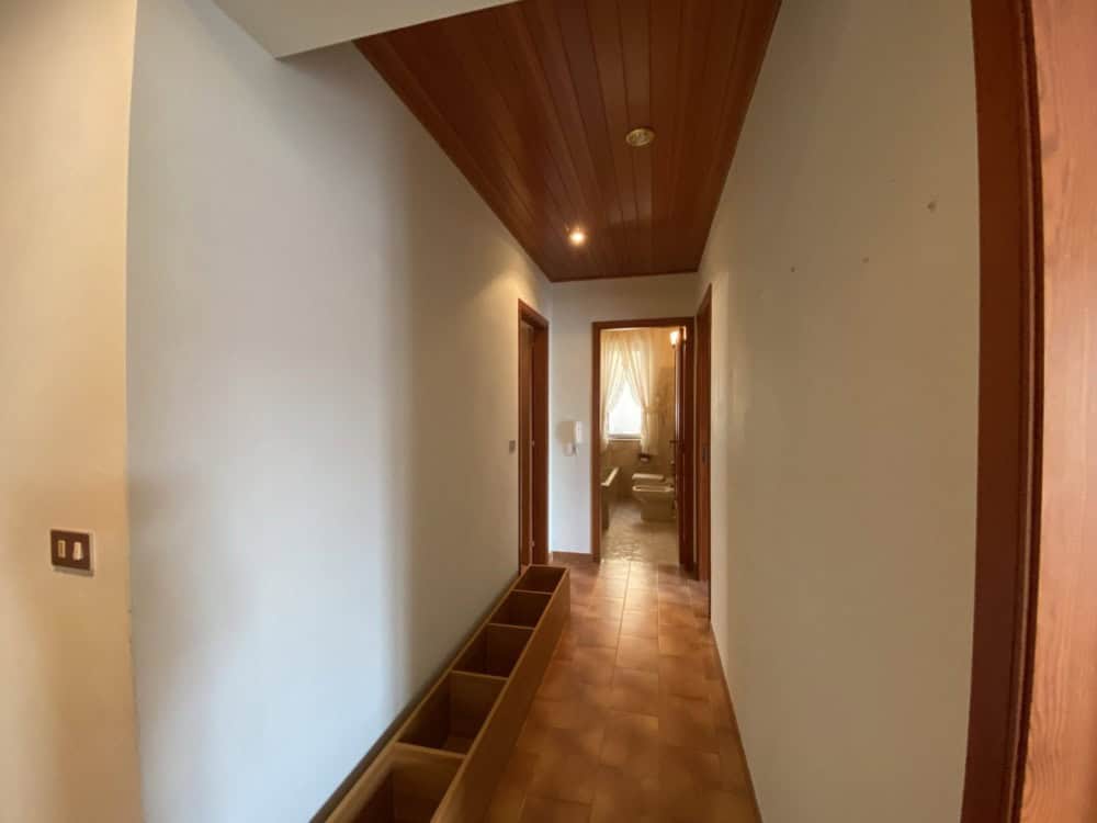 Porte di ingresso in legno in un corridoio luminoso con pareti bianche e pavimento in piastrelle, ambiente accogliente e ben illuminato.