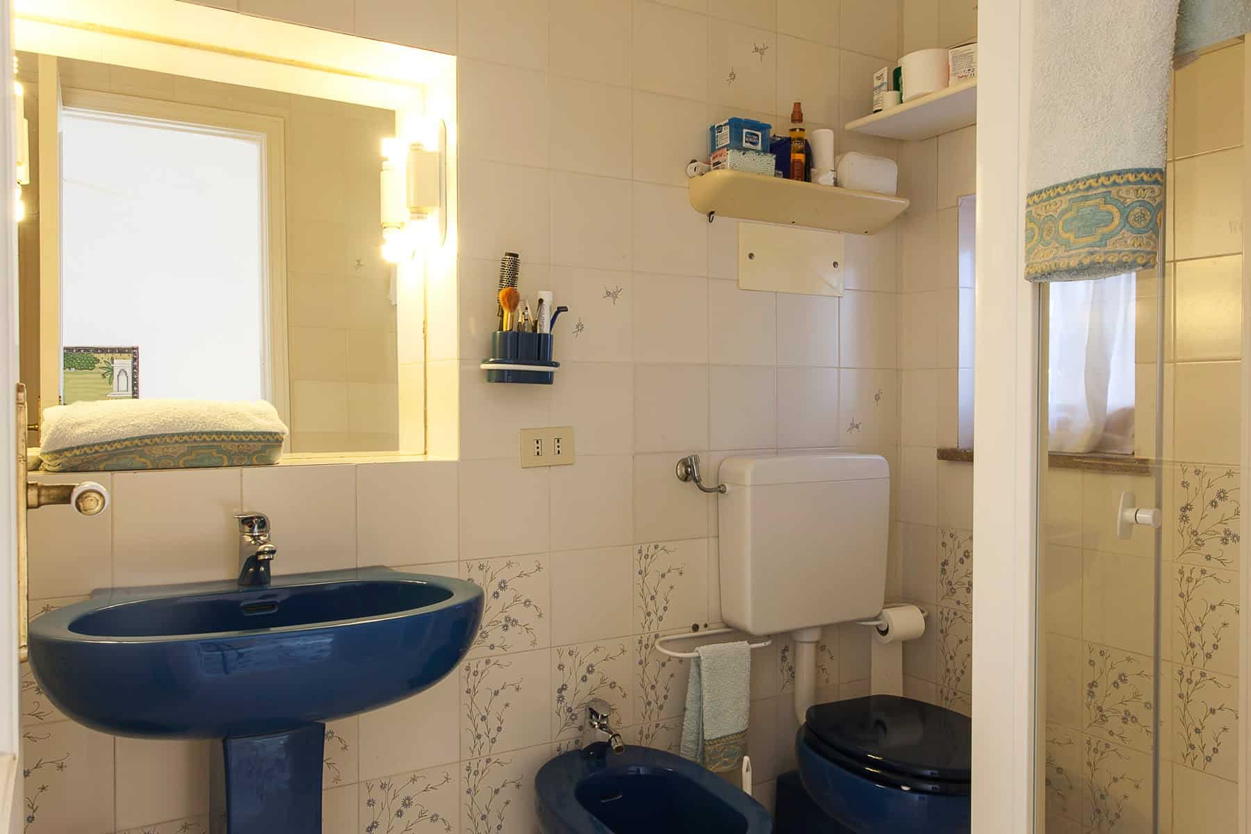 Il lavabo e il water blu in un bagno con pareti bianche e accessori essenziali.
