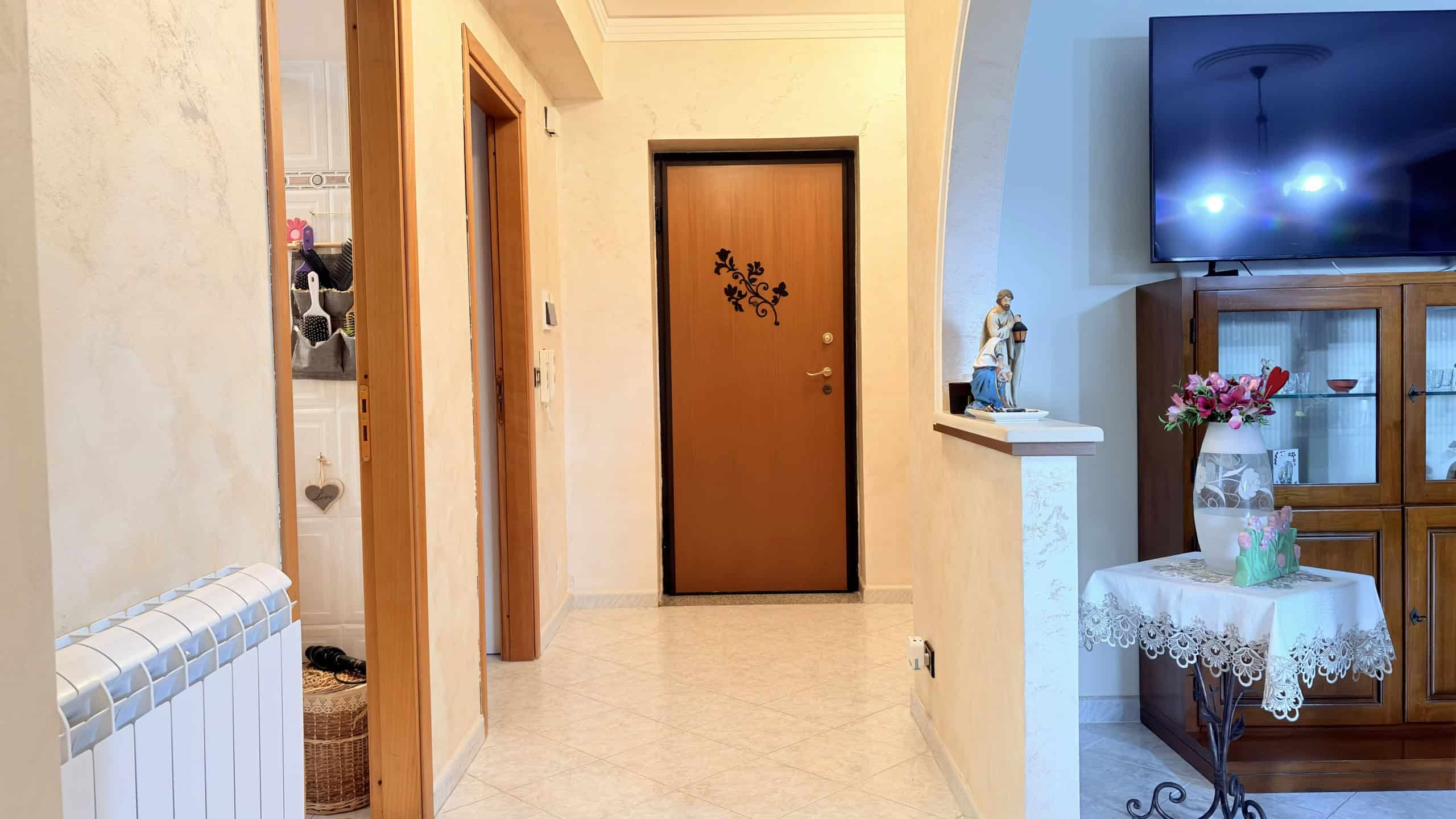 Porta d'ingresso in legno con decorazioni floreali, situata in un ingresso di casa accogliente e ben illuminato, con pareti color crema e pavimento in piastrelle lucide.