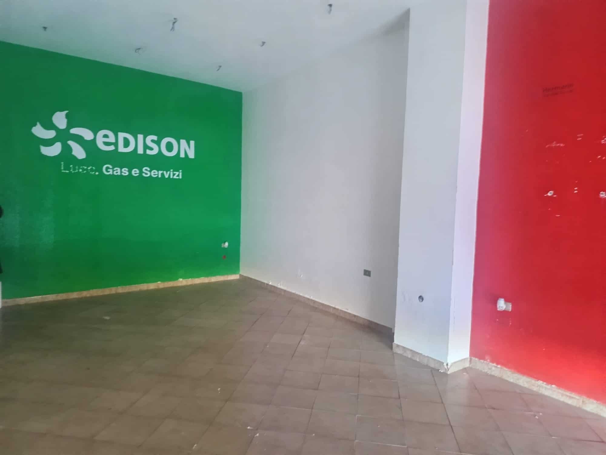 Pompa di gas Edison in un ambiente commerciale con pareti verdi e rosse, pavimento in piastrelle, spazio vuoto e segnale pubblicitario per servizi di luce, gas e energia.