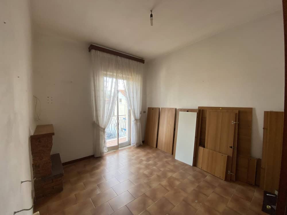 Una stanza vuota con pareti bianche, pavimento in piastrelle e una finestra con tende leggere che permette l'ingresso di luce naturale, pronta per essere arredato e personalizzato.