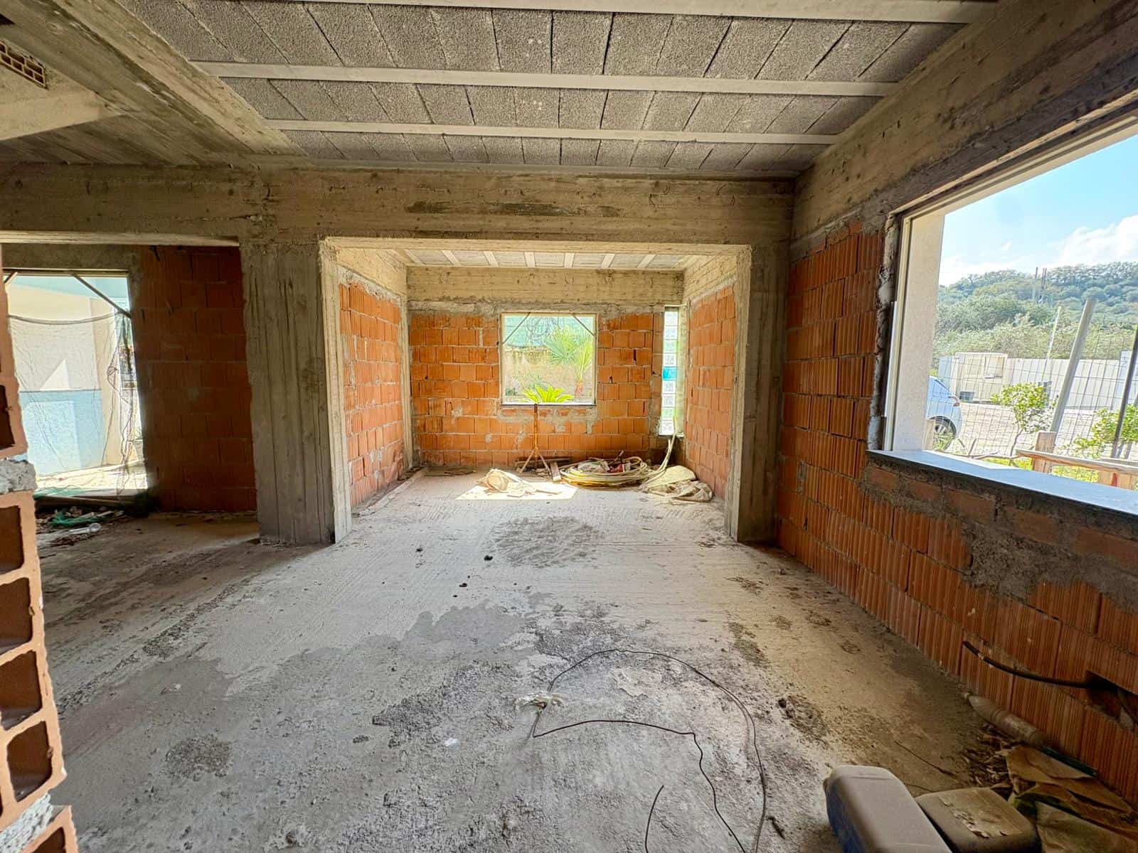 Cantiere edile con struttura in cemento e mattoni, vista interna di un edificio in costruzione con grandi finestre e vista panoramica sulla natura circostante.