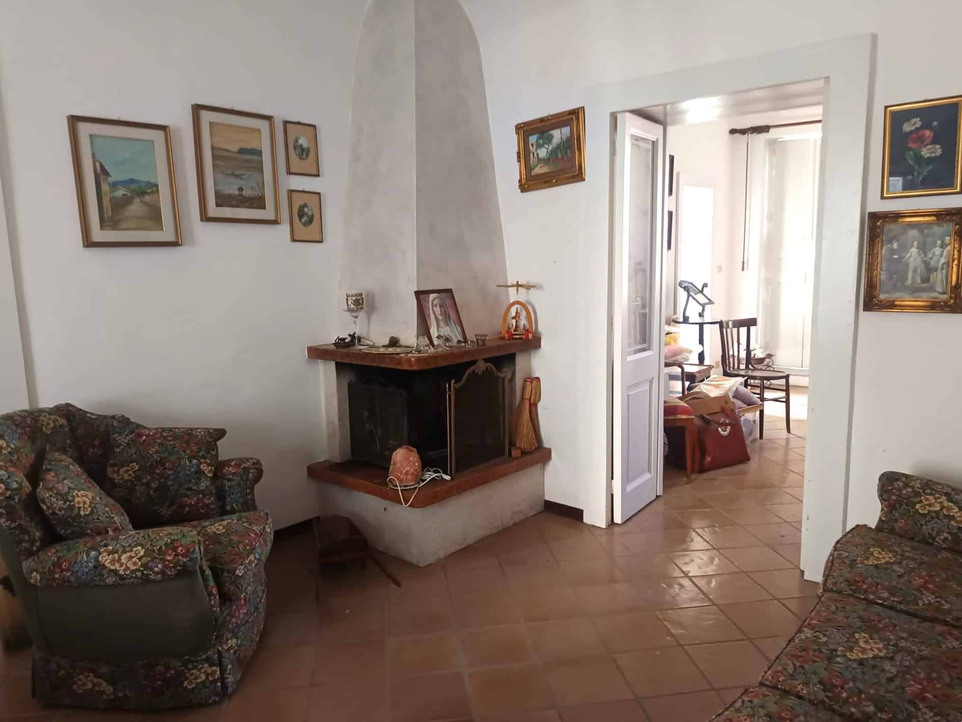Ampio soggiorno con camino, arredato con divani fiorati e decorazioni alle pareti, in stile classico e accogliente, ideale per momenti di relax e convivialità.