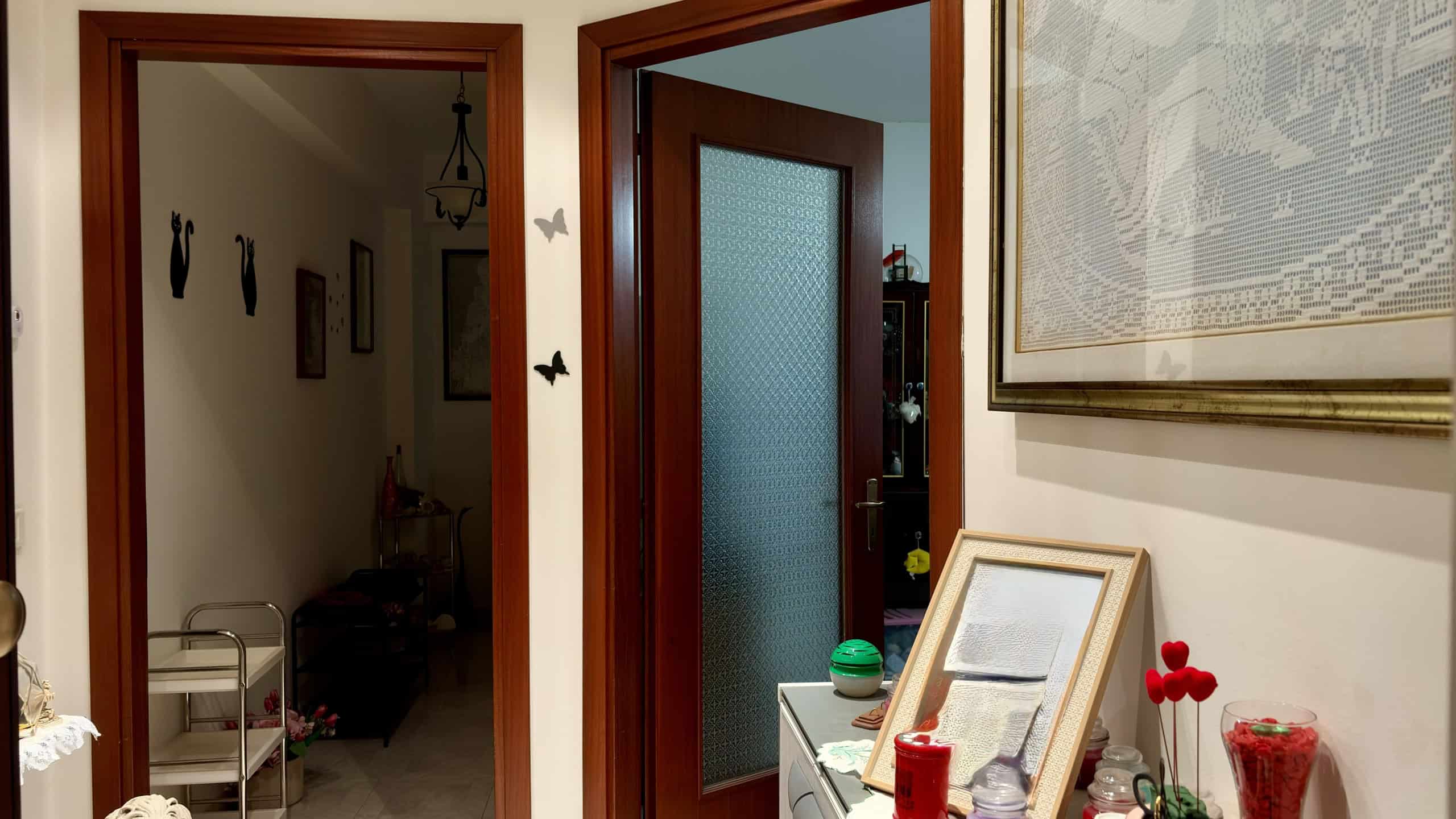 L'immagine mostra un ingresso di casa con porta in legno e vetro satinato, arredato con dettagli decorativi e oggetti di uso quotidiano, creando un ambiente accogliente e funzionale.