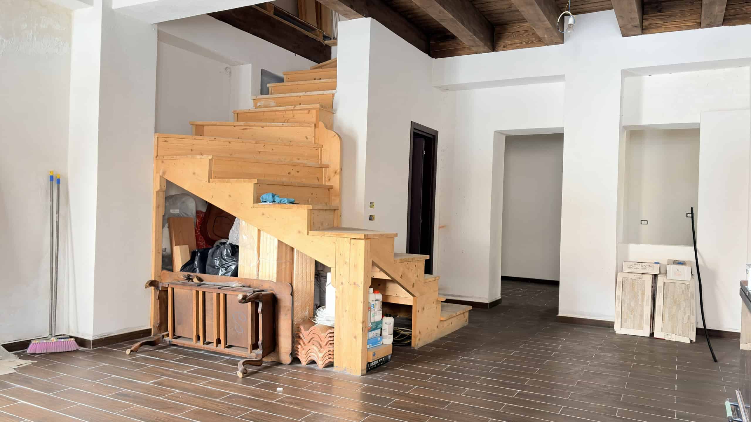 Scale in legno in fase di installazione all'interno di un appartamento moderno, con pareti bianche e soffitto in legno a vista, pronto per essere completato.