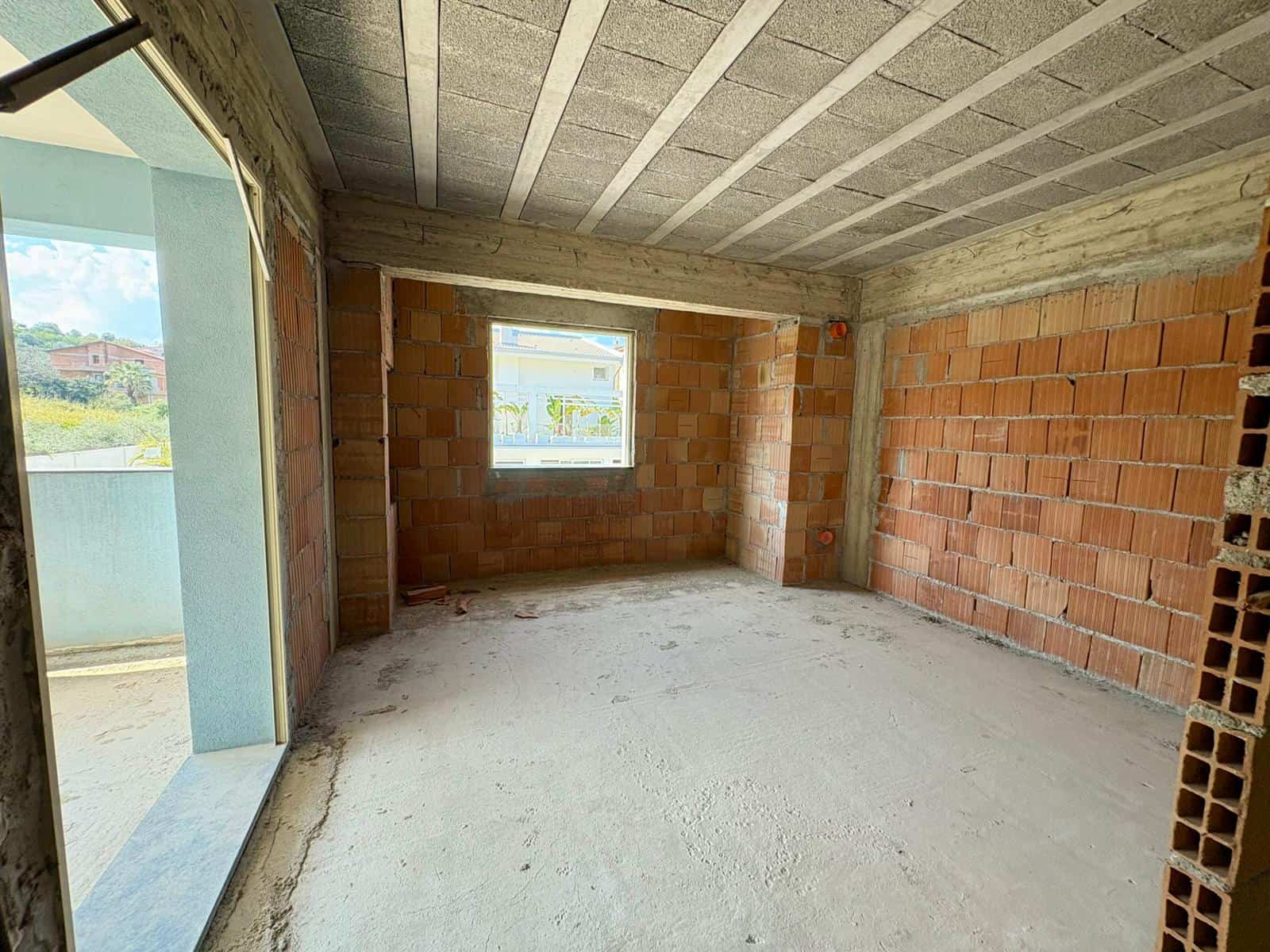 Appartamento in costruzione con pareti in mattoni e grandi finestre, pronto per essere rifinito, ideale per chi cerca una casa personalizzabile in zona residenziale.