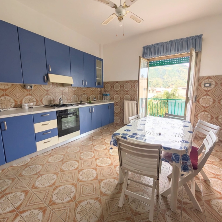 Lavastoviglie e cucina moderna in una cucina spaziosa con pareti rivestite di piastrelle colorate, tavolo da pranzo con sedie e accesso a un balcone con vista panoramica.