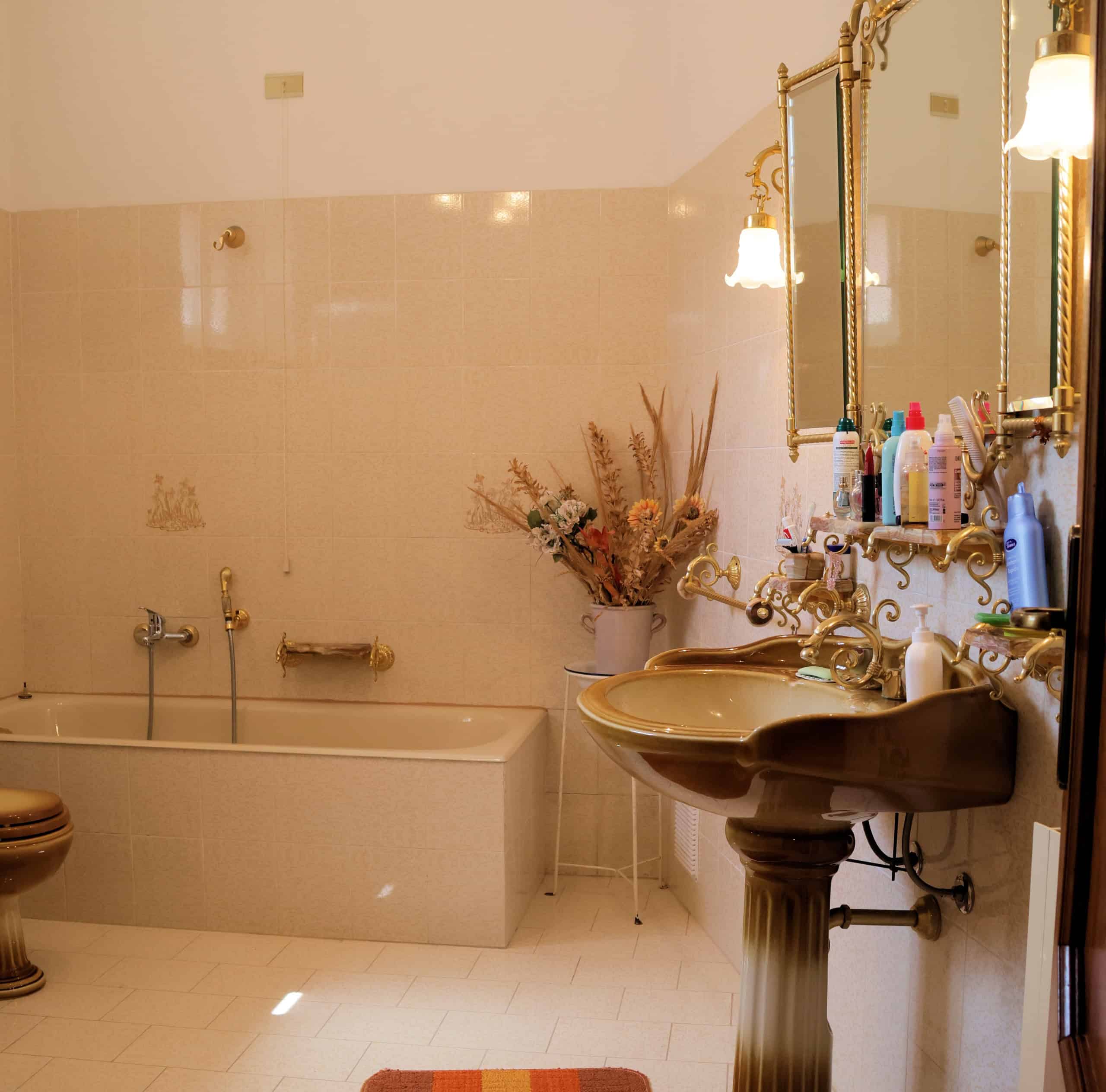 Il lavabo antico con specchio dorato in un bagno classico, decorato con fiori secchi e prodotti per la cura personale, crea un ambiente elegante e accogliente.