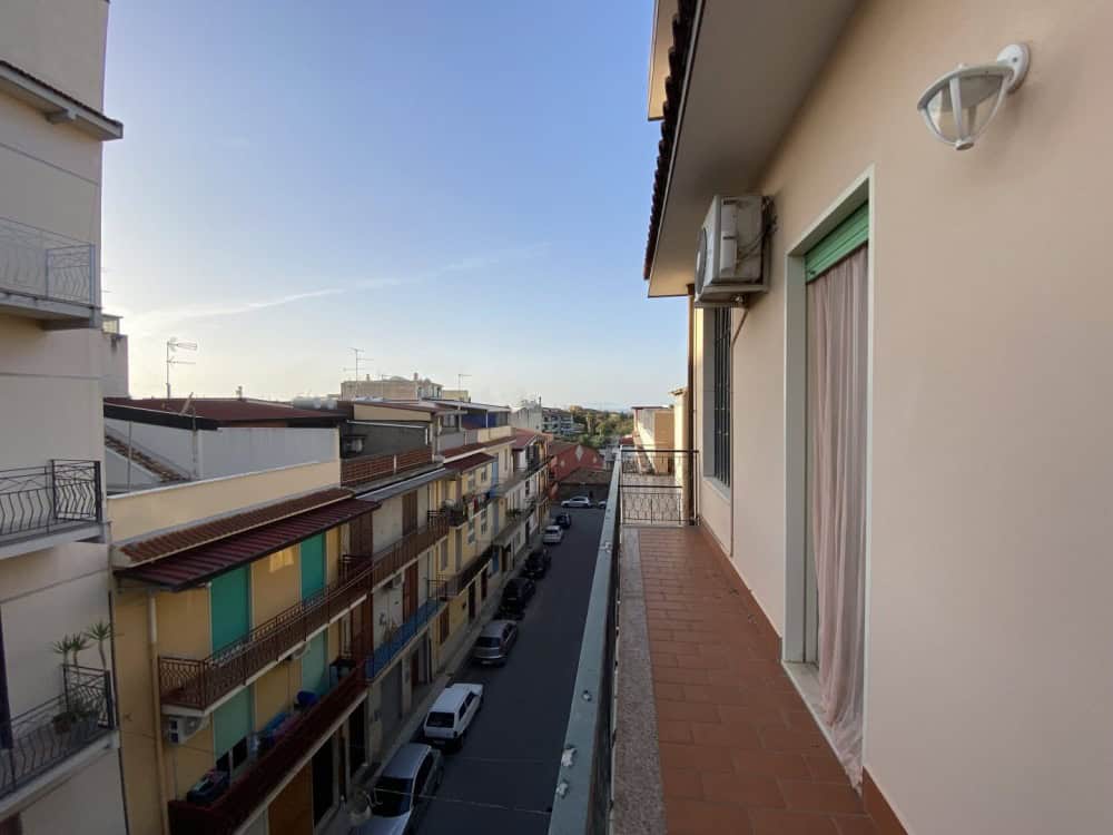 Balcone di un appartamento con vista su strada urbana, edifici residenziali e cielo sereno, in un quartiere tranquillo e ben servito, ideale per vivere in città con comfort e comodità.
