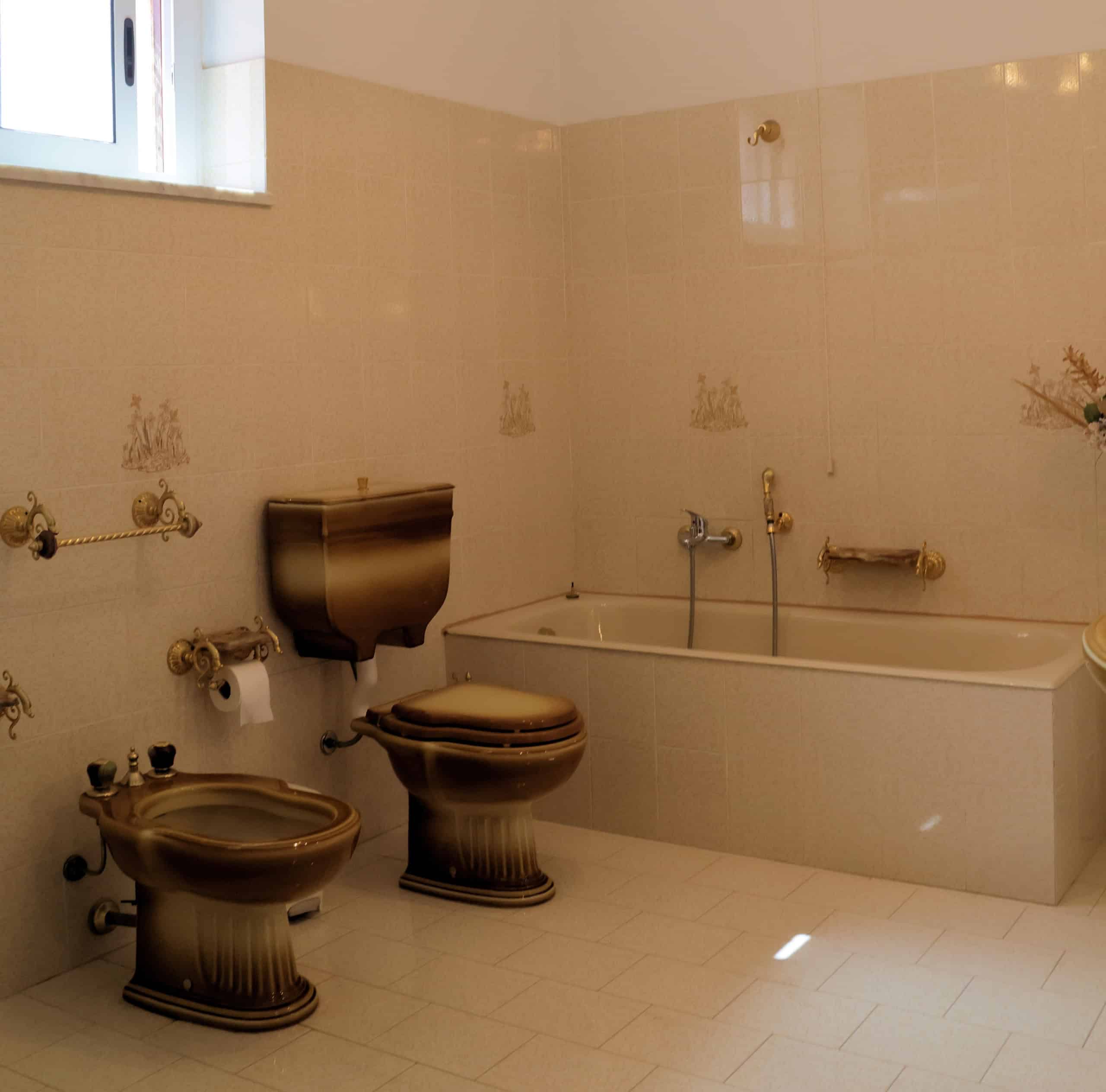 Lavabo e bidet vintage in bagno con vasca, stile classico e dettagli decorativi in ceramica beige. Ambiente luminoso con finestra e piastrelle decorate. Perfetto per un bagno elegante e funzionale.