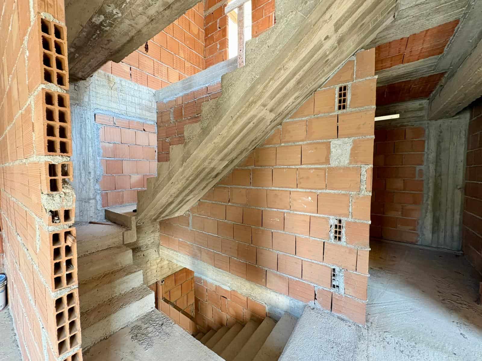Scale in costruzione di un edificio residenziale con pareti in mattoni rossi e struttura in cemento armato, evidenziando i dettagli delle fondamenta e delle scale interne.