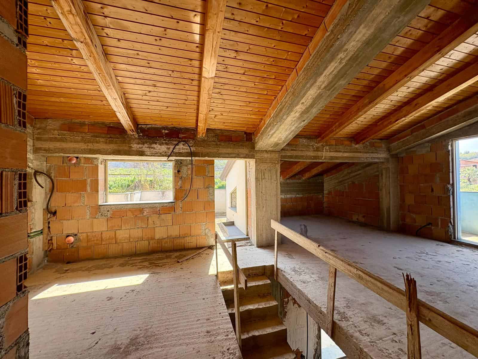 Tetto in fase di costruzione con travi in legno e pareti in mattoni, spazio interno di un edificio in costruzione, luce naturale che entra attraverso le finestre.