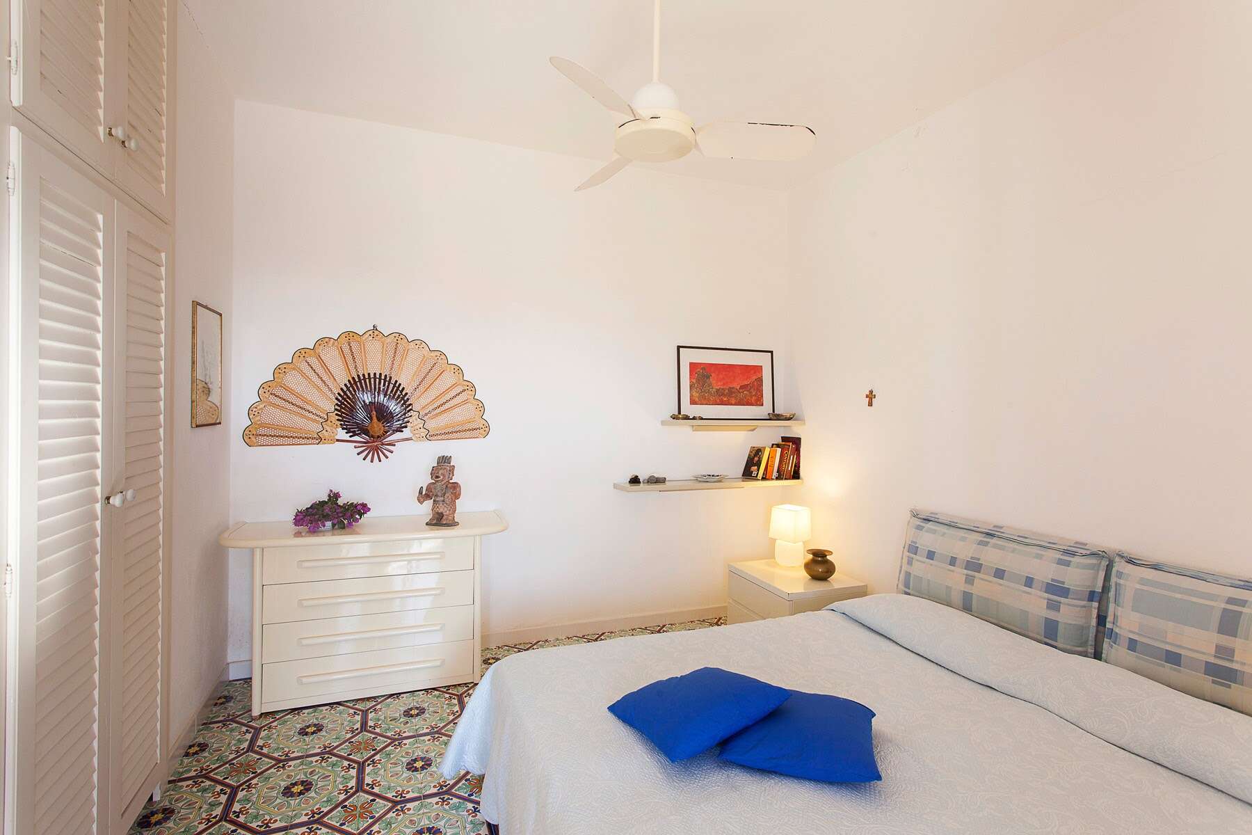 Una stanza da letto luminosa e accogliente con pareti bianche, decorazioni eleganti e un letto con lenzuola a quadri blu e bianche, ideale per ambienti di case in vendita o affitto.