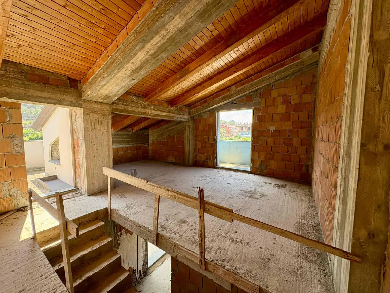 Pannello di soffitta in costruzione con struttura in legno e mattoni rossi, spazio ancora da rifinire, con vista sulla città e sul paesaggio circostante.