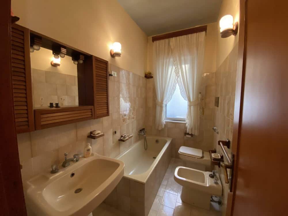 Lavabo e vasca da bagno in un bagno classico con illuminazione calda e tende leggere alla finestra.