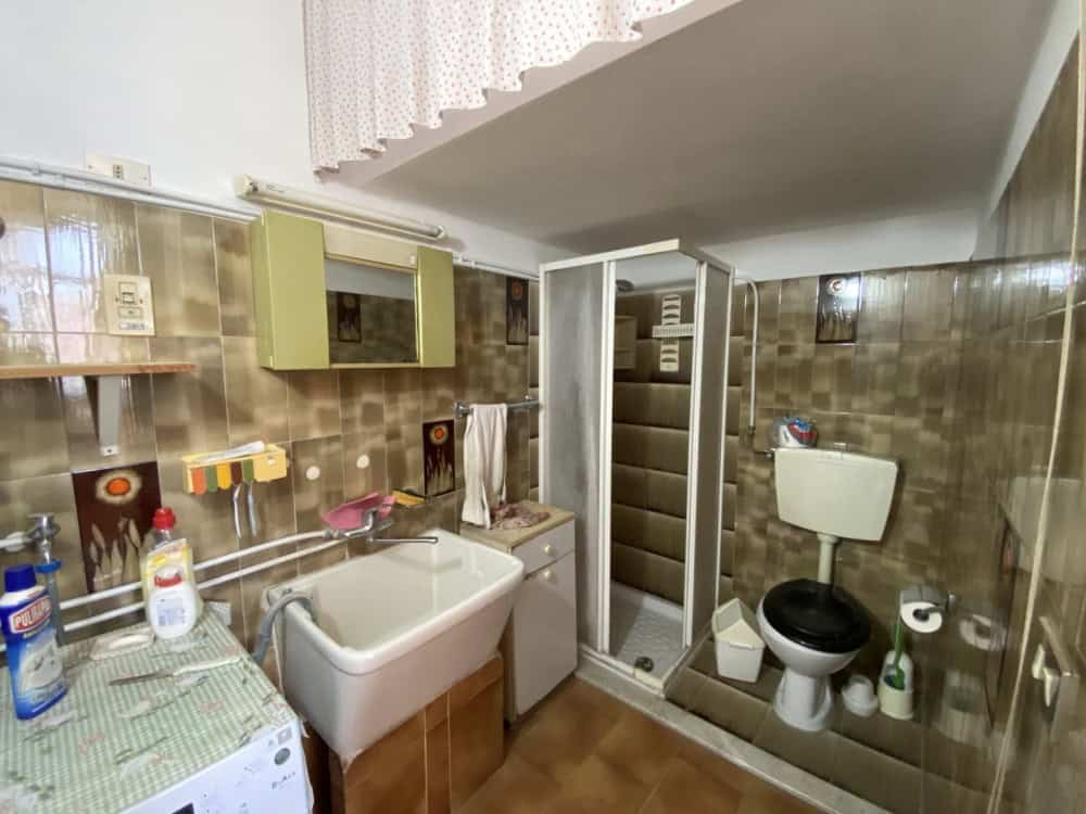 Lavanderia con lavatrice, lavabo e doccia in un ambiente domestico con pareti rivestite in piastrelle marroni e soffitto inclinato. Spazio funzionale per le faccende domestiche e il bucato.