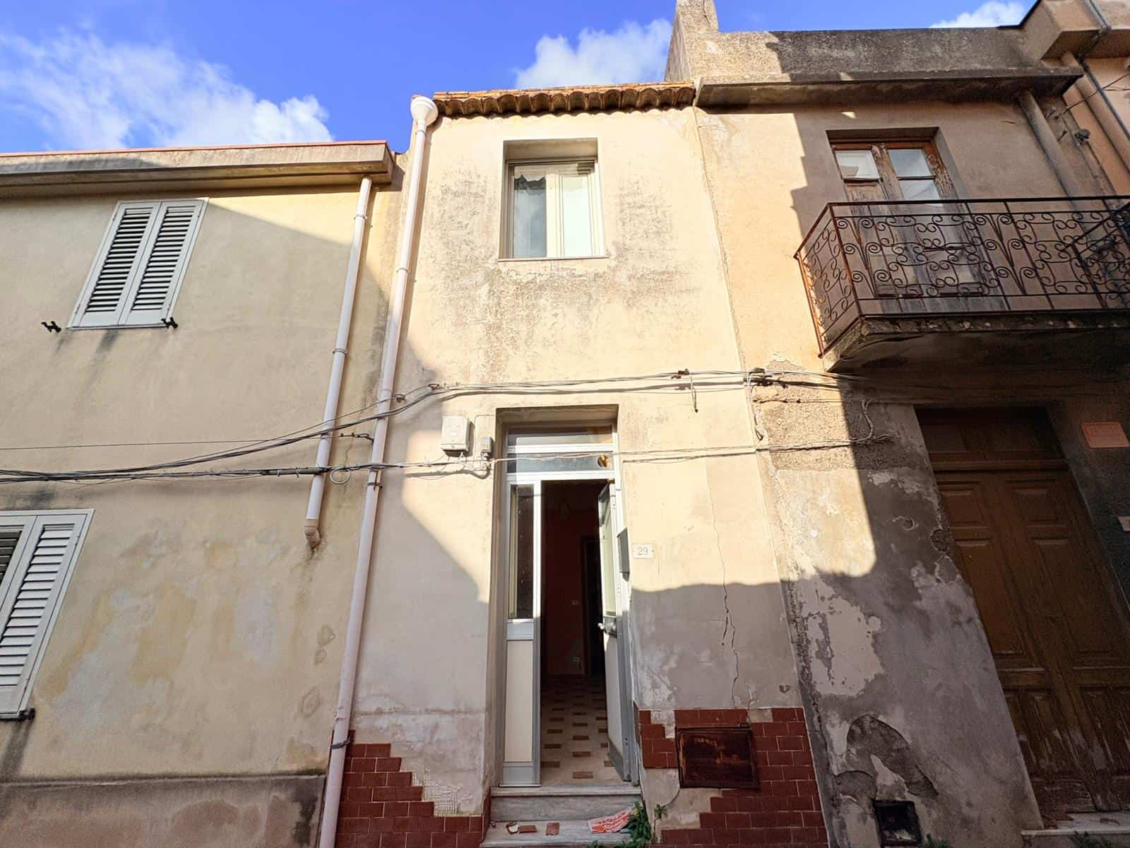Vicolo di case storiche con facciate in pietra e balcone in ferro battuto, in un quartiere tradizionale italiano. Edificio residenziale con caratteristiche architettoniche autentiche e atmosfera tipic.