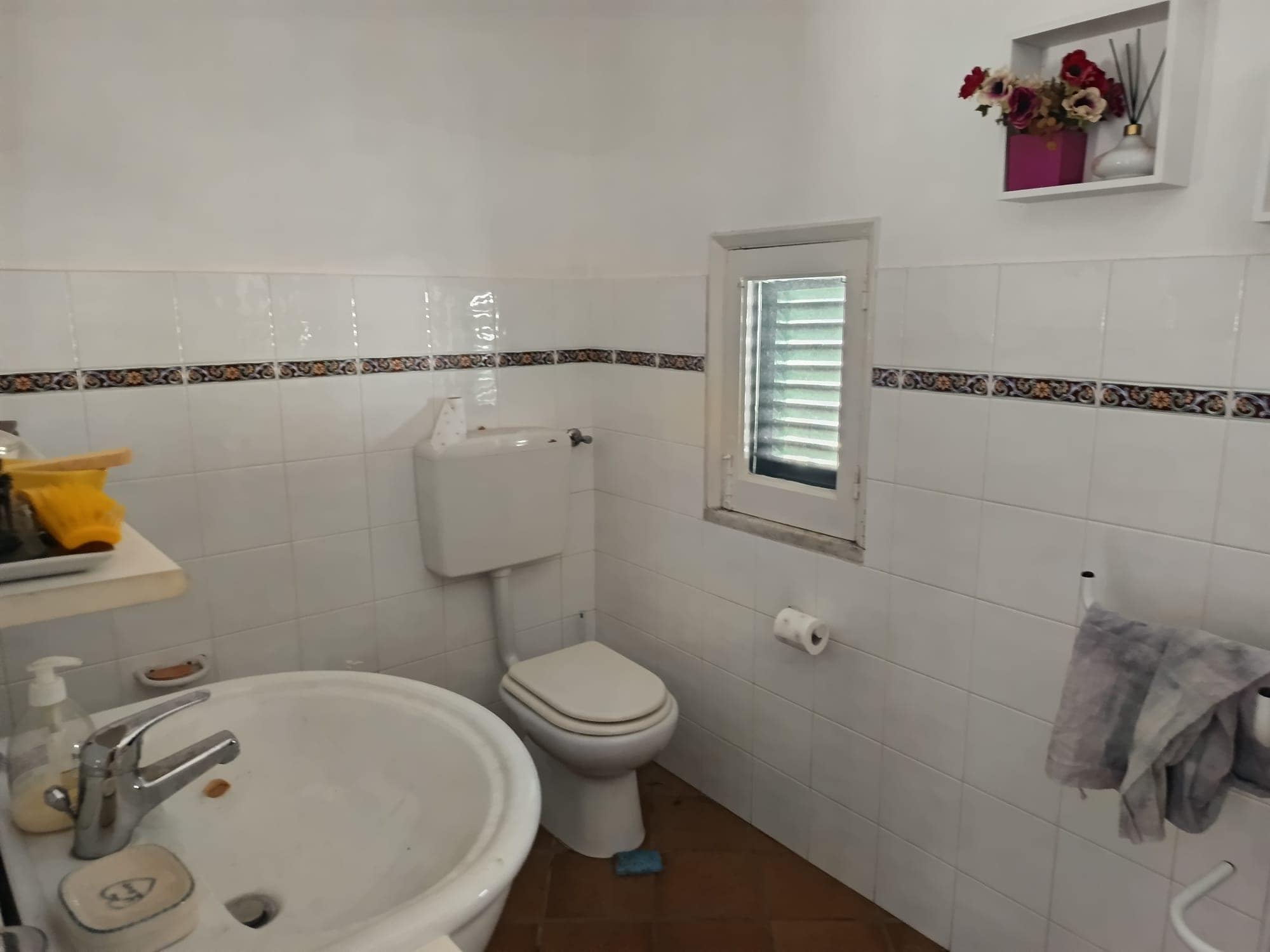 Lavabo e servizi igienici in bagno con finestra e decorazioni floreali, ambiente pulito e funzionale.