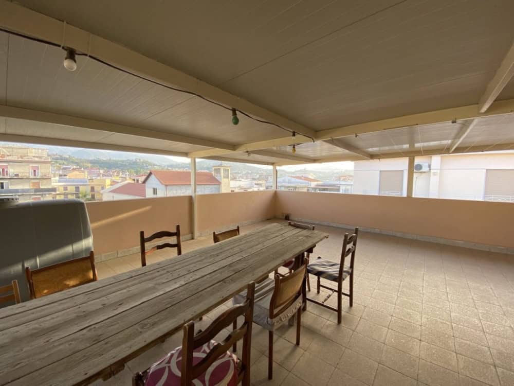 Ampia terrazza coperta con tavolo in legno e sedie, vista panoramica sulla città, ideale per pranzi all'aperto e momenti di relax, ambiente luminoso e spazioso.