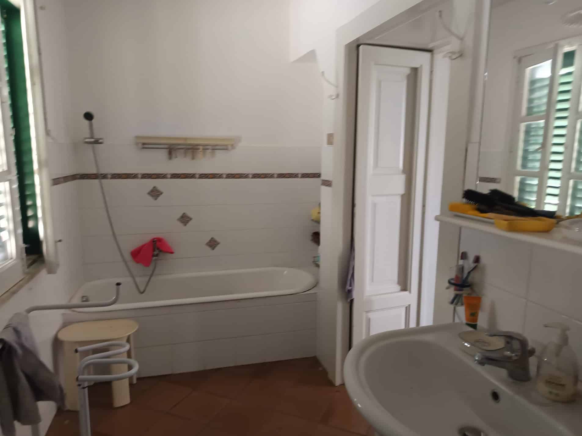 Il bagno di una casa con vasca, lavabo e finestra con persiane verdi, arredato in modo semplice e funzionale, ideale per ambienti residenziali e ristrutturazioni di case.