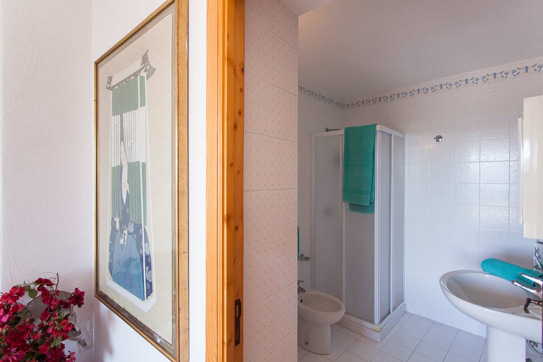 Lavabo e cabina doccia in bagno con pareti bianche e accessori azzurri, in un ambiente luminoso e pulito.