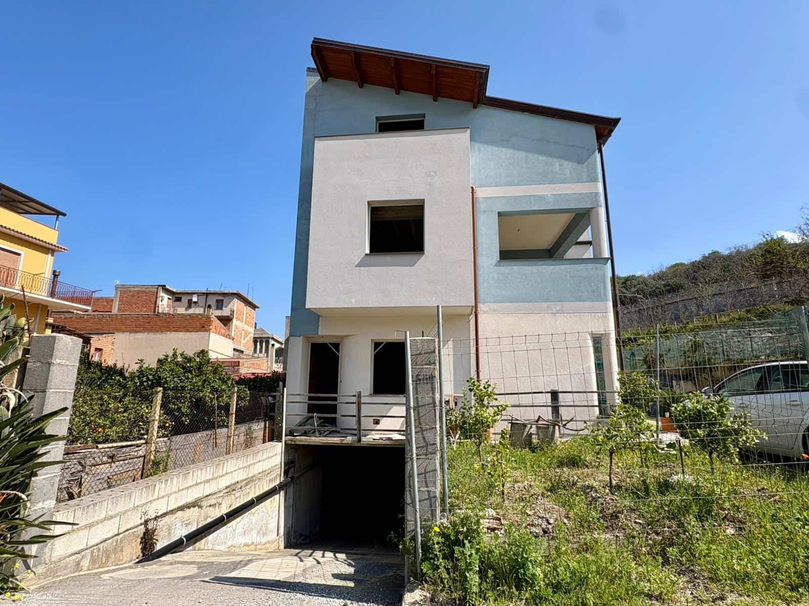 Casa moderna a tre piani con garage interrato, balcone e giardino, situata in zona residenziale soleggiata, con vista sulle colline circostanti.