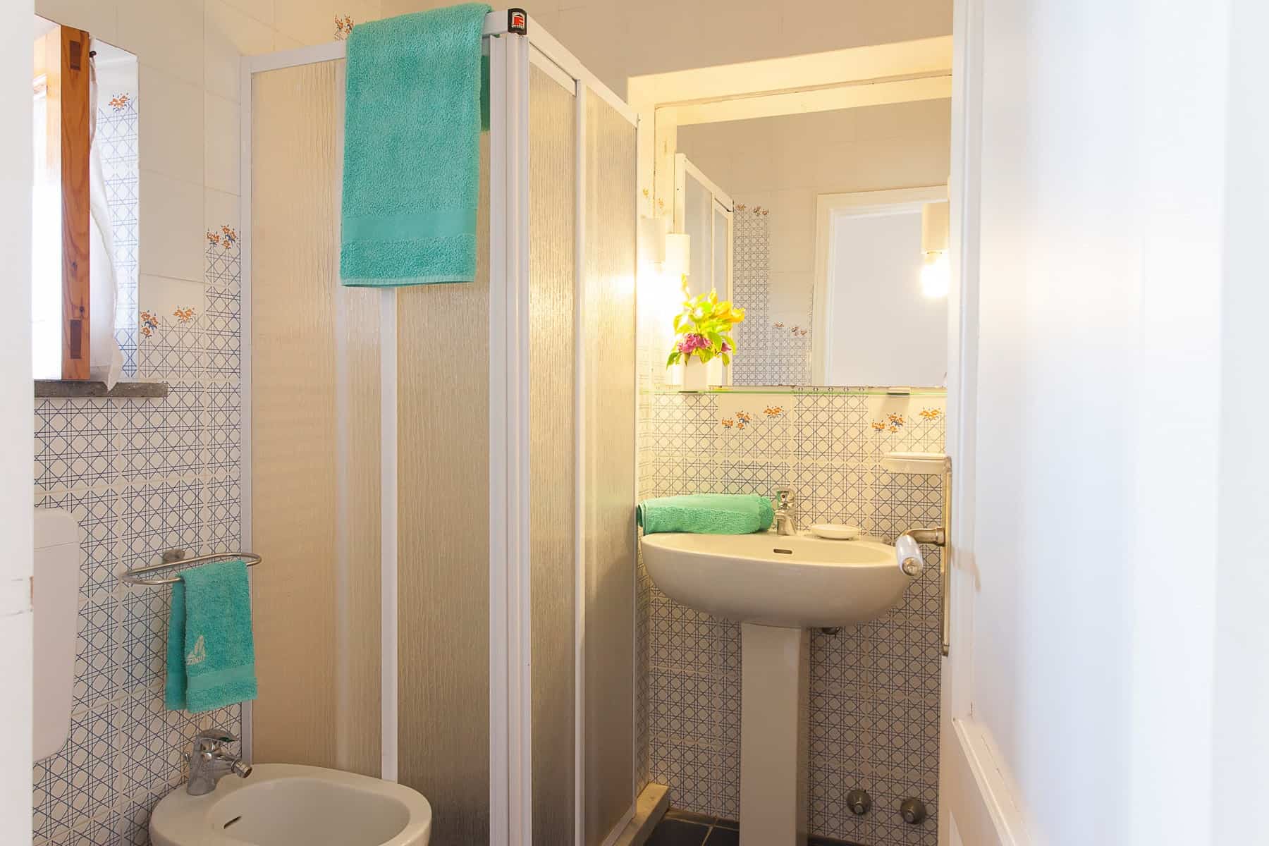 Lavabo e doccia in un bagno compatto con accessori turchesi, specchio e illuminazione calda, ideale per soluzioni abitative moderne e funzionali.