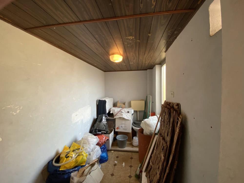 Spazio di stoccaggio in soffitta con scatole, materiali e oggetti vari, illuminato da luce calda, con soffitto in legno e pareti bianche, pronto per organizzazione o ristrutturazione.