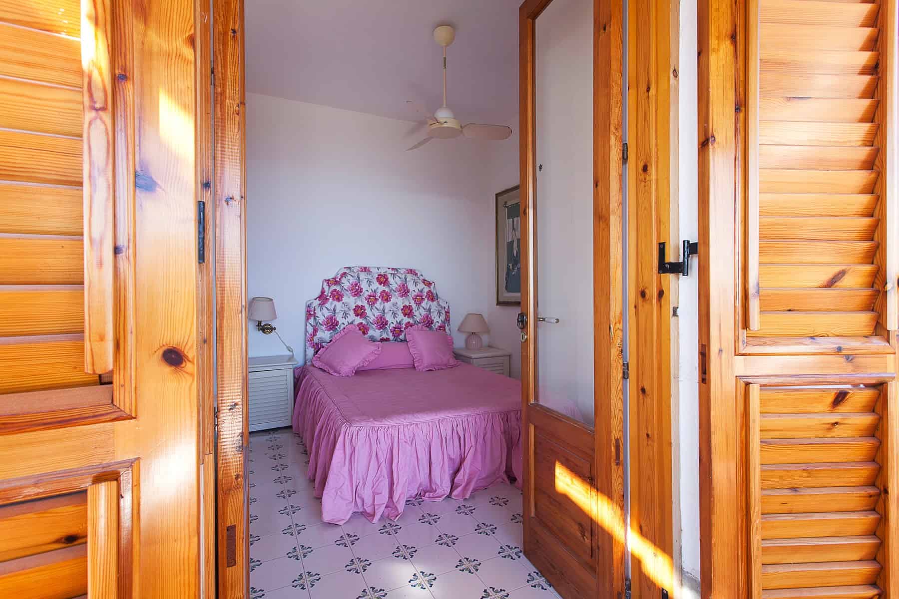 Ampio soggiorno con porte in legno, camera da letto con letto matrimoniale e decorazioni floreali, illuminazione naturale, ideale per case vacanza e affitti turistici.
