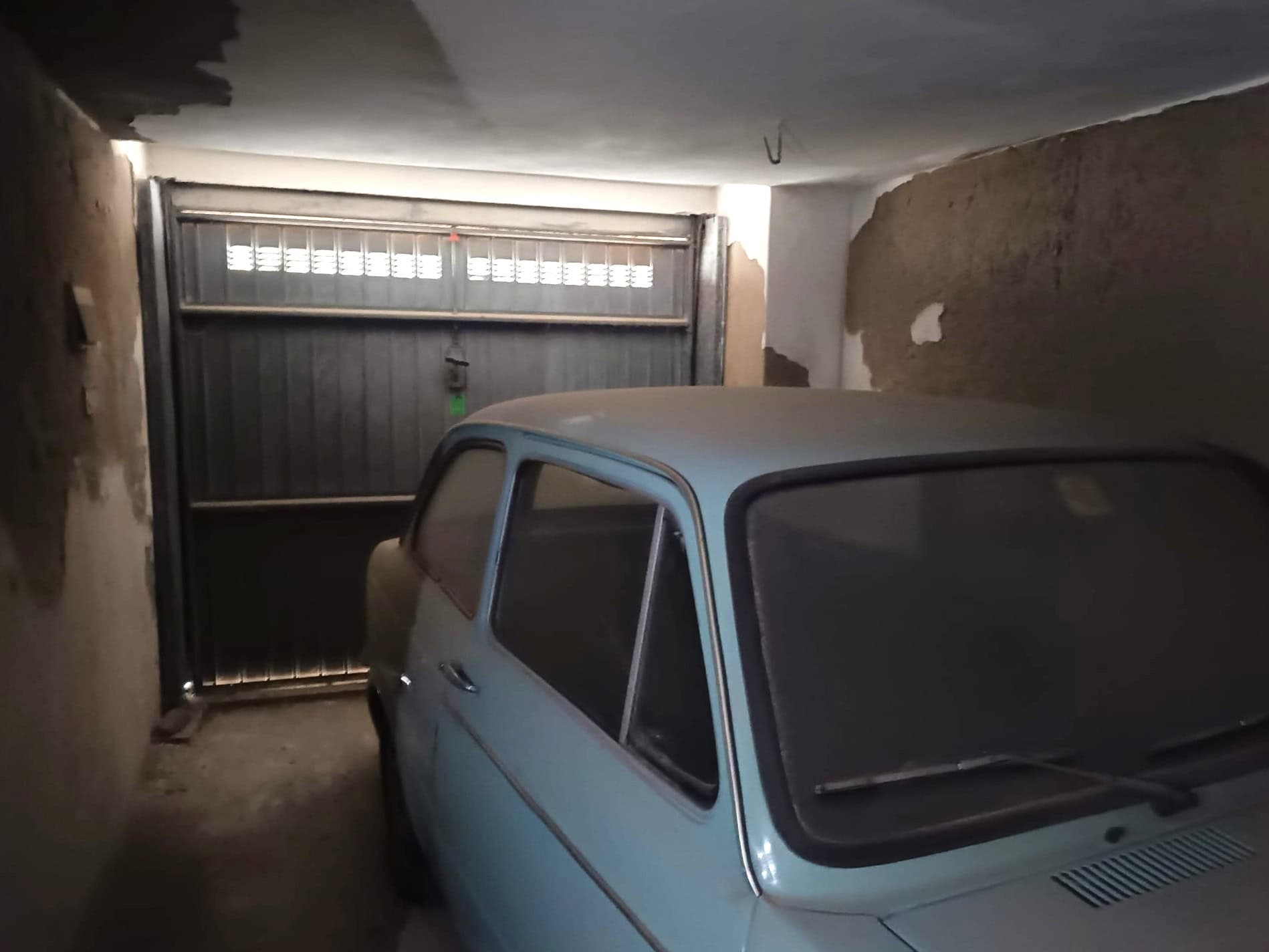 Auto d'epoca parcheggiata in un garage sotterraneo con pareti in cemento e porta automatica.