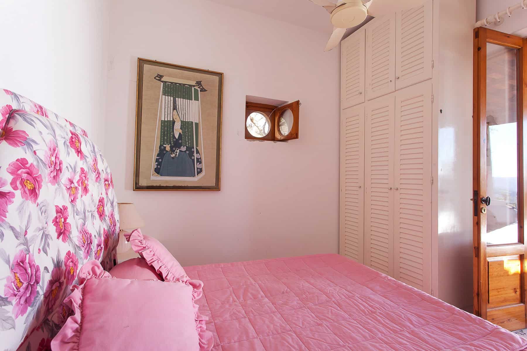 Aria di camera da letto luminosa con pareti bianche, letto con copriletto rosa e cuscini coordinati, armadio a muro bianco e finestra con vista all'aperto, decorazioni eleganti e atmosfera accogliente.