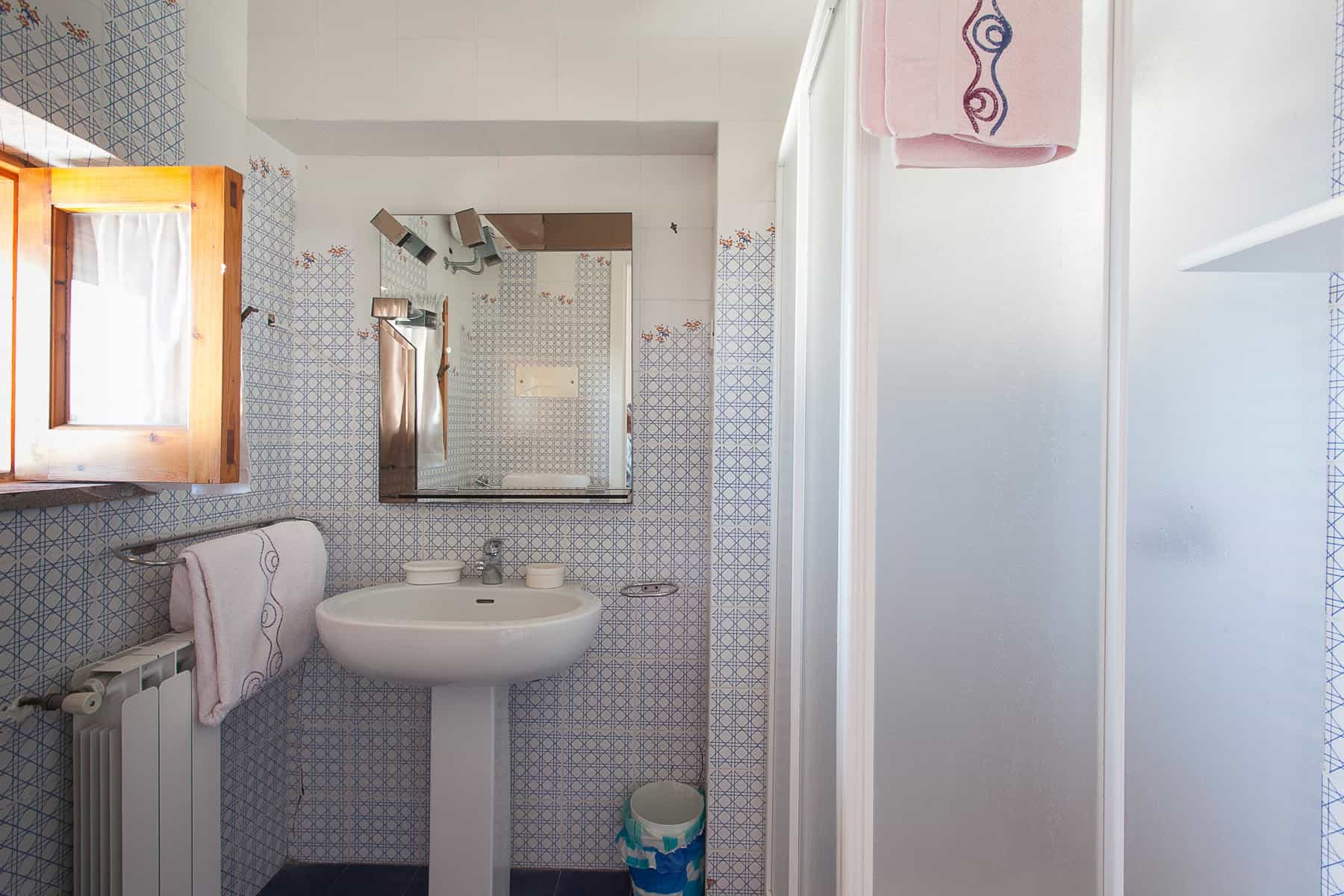 Lavabo e specchio in un bagno con piastrelle azzurre e dettagli rosa, ambiente luminoso e pulito.