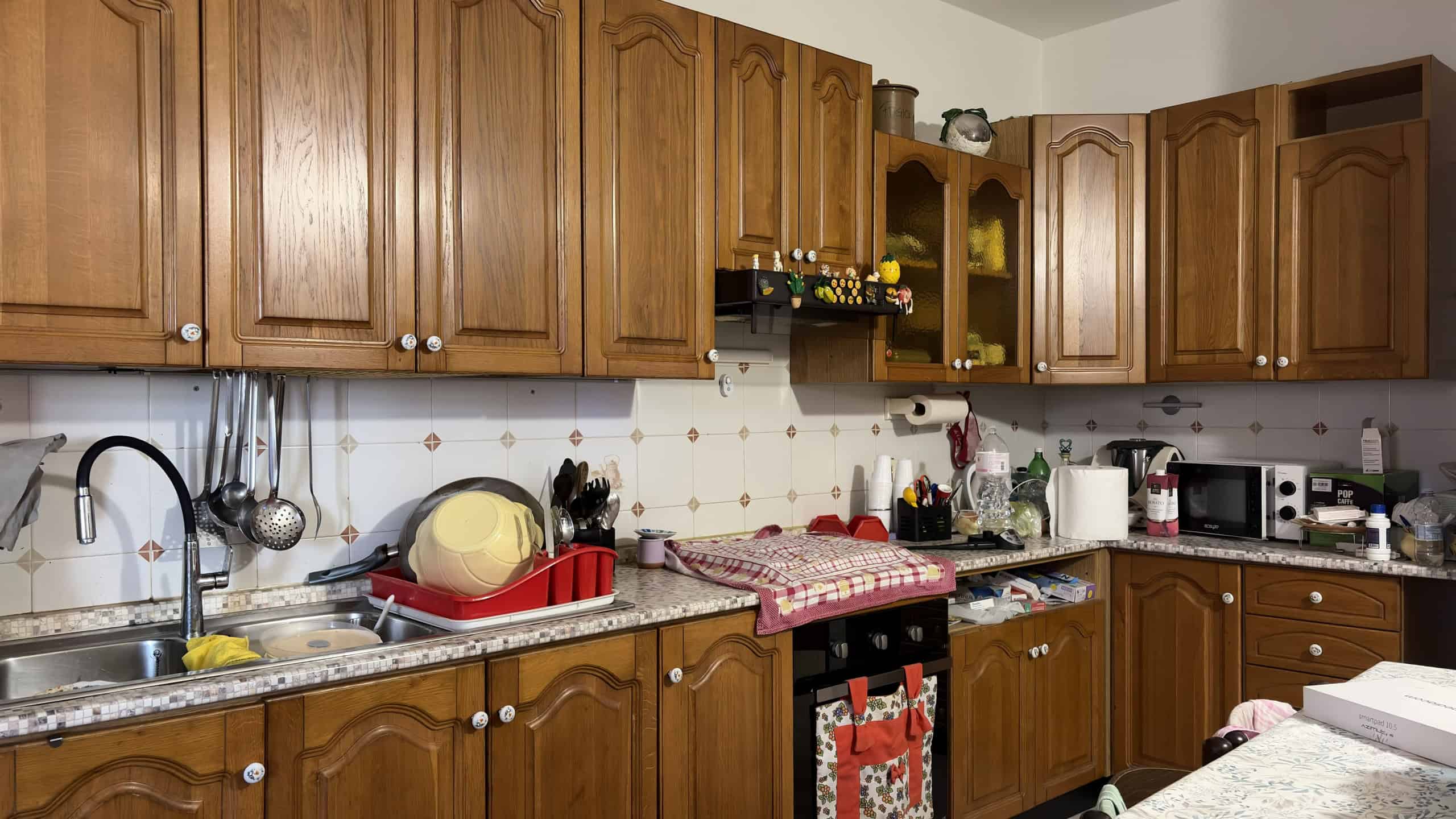 Lavandino e piano di lavoro in cucina con mobili in legno, utensili e elettrodomestici, ambiente domestico accogliente e funzionale.