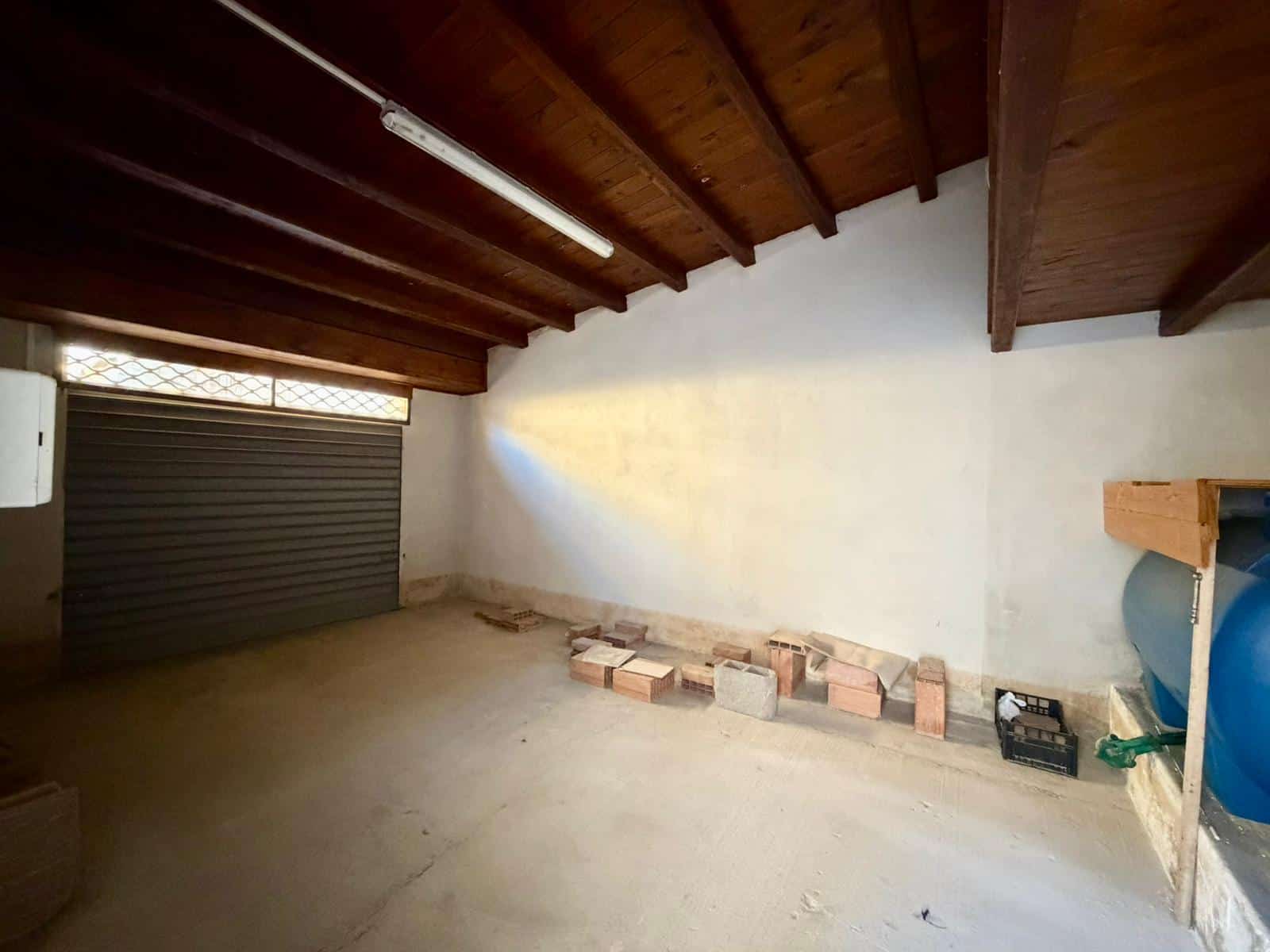 Soffitta spaziosa con soffitto in legno e pareti bianche, ideale come deposito o spazio di lavoro, con accesso tramite porta basculante e pavimento in cemento.
