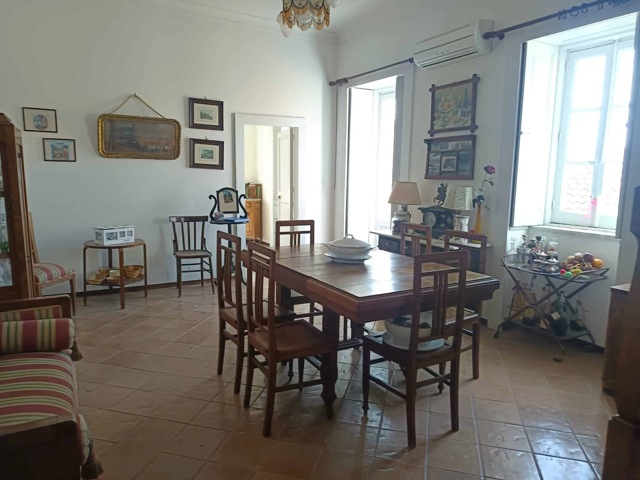 Anticamera soggiorno con tavolo in legno, sedie e decorazioni vintage, ambiente luminoso e accogliente, ideale per vivere momenti di convivialità e relax.