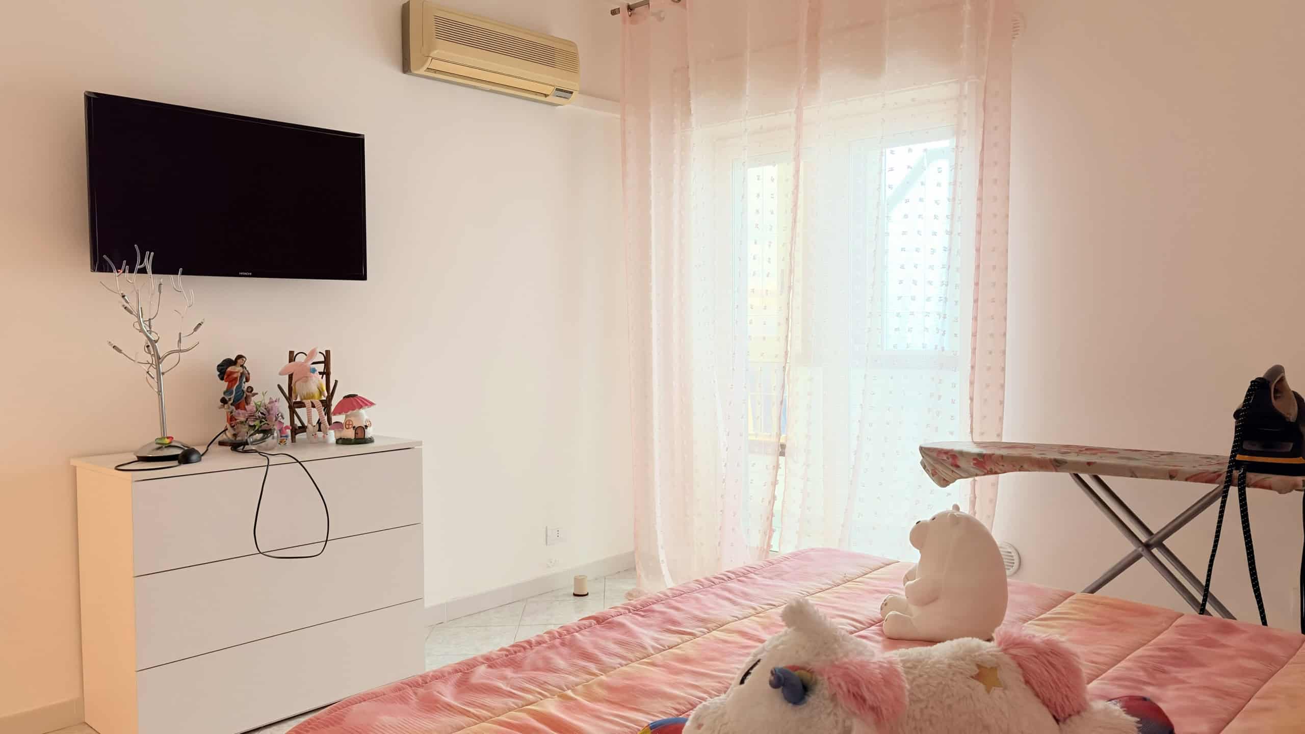 Ampio soggiorno con parete attrezzata, TV a schermo piatto, aria condizionata, e zona relax con letto e oggetti decorativi, ideale per vivere in comfort e stile.