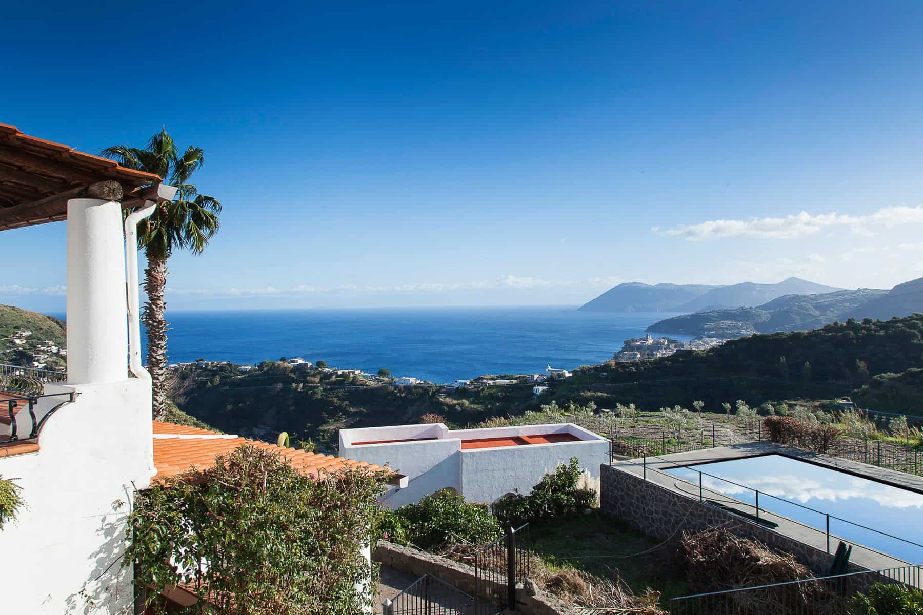 Vista panoramica sul mare e sulle colline con case bianche e piscina, paesaggio mediterraneo, cielo sereno, natura e relax, immobile di lusso in vendita a NextCasa.