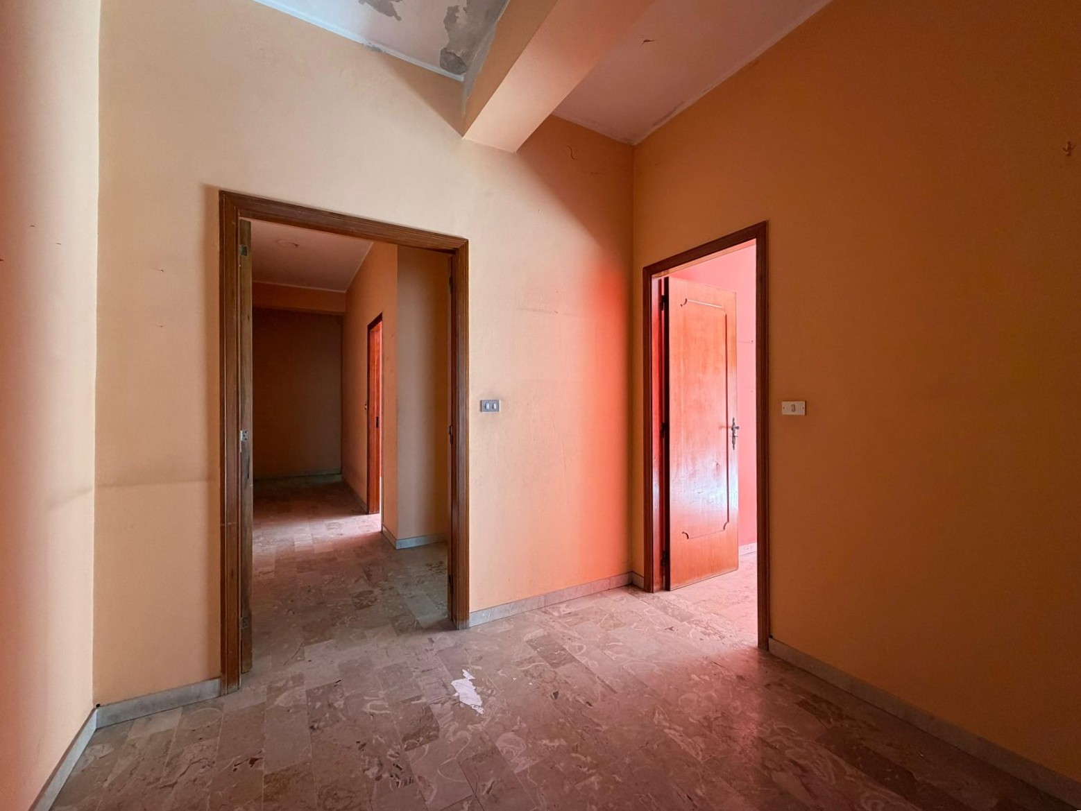Appartamento in fase di ristrutturazione con pareti arancioni e porte in legno, ingresso spazioso e luminoso, ideale per creare un ambiente accogliente e moderno. Perfetto per investimenti immobiliari.